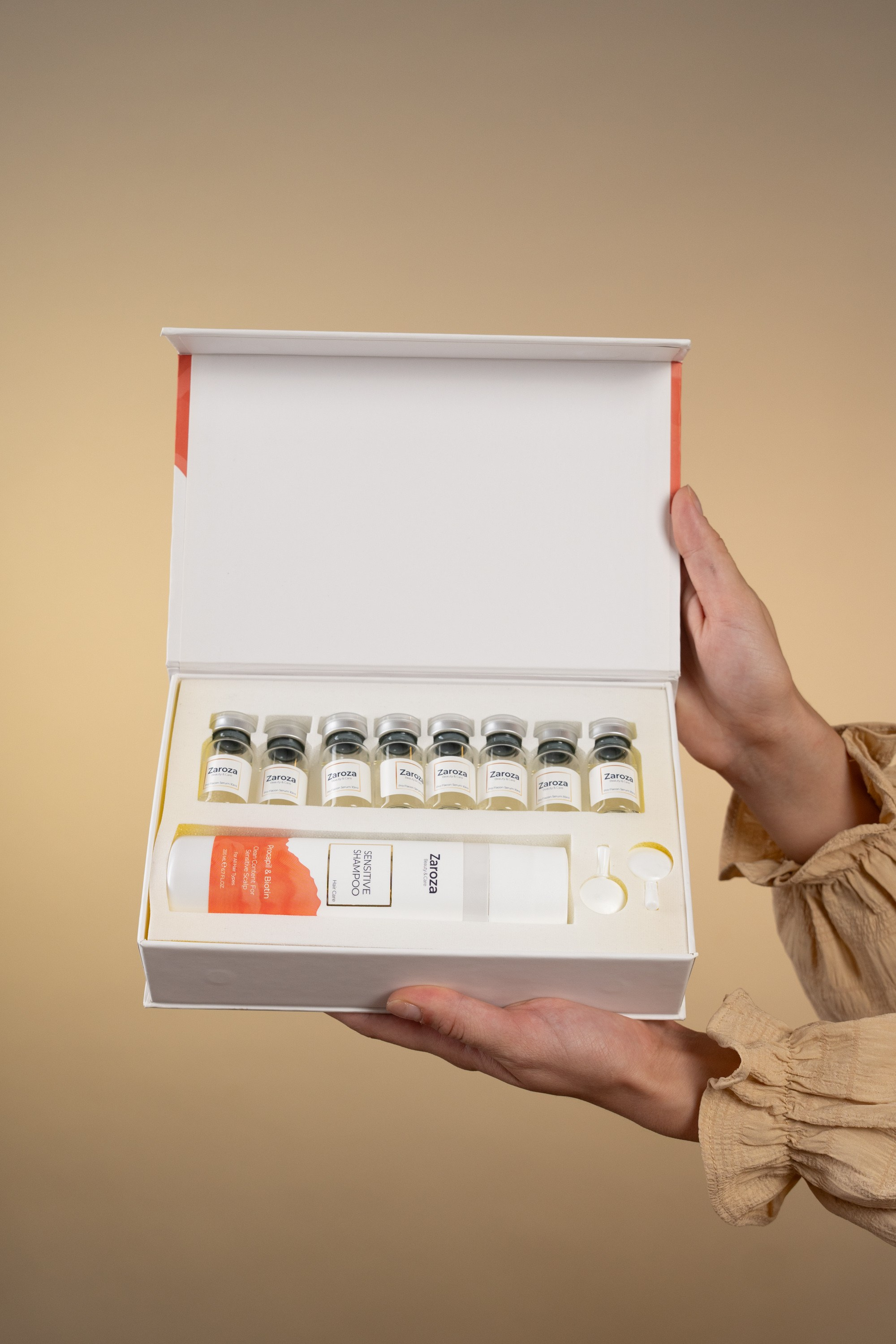 Zarozanın saç baxımı dəsti – ampulalar və Sensitive Shampoo olan ağ qutu, bej fonda təqdimat.