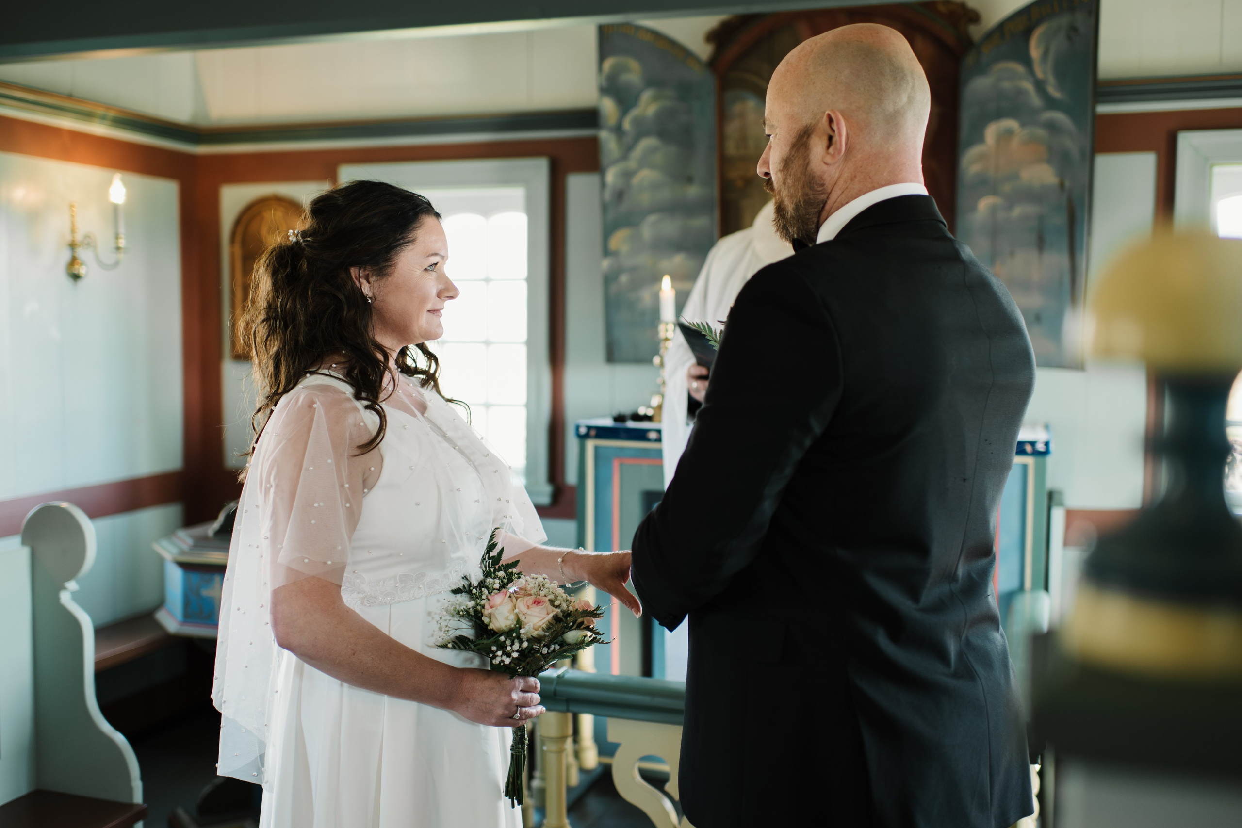 Intimate embrace between the bride and groom near the black church of Búðir, framed by rolling hills and an overcast sky.