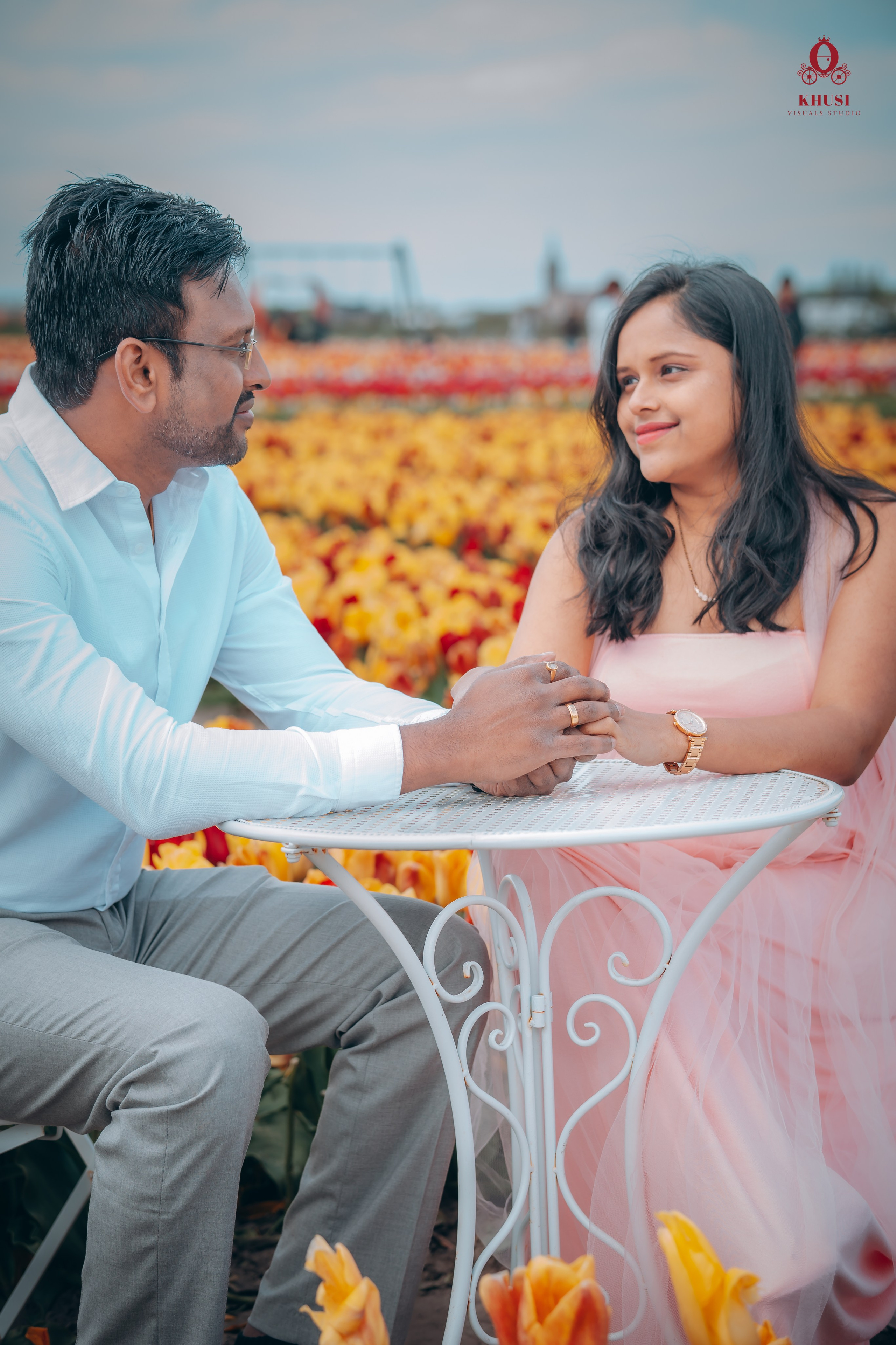A pregnant couple sitting on a tea table and holding hands in a tulip field in Netherlands