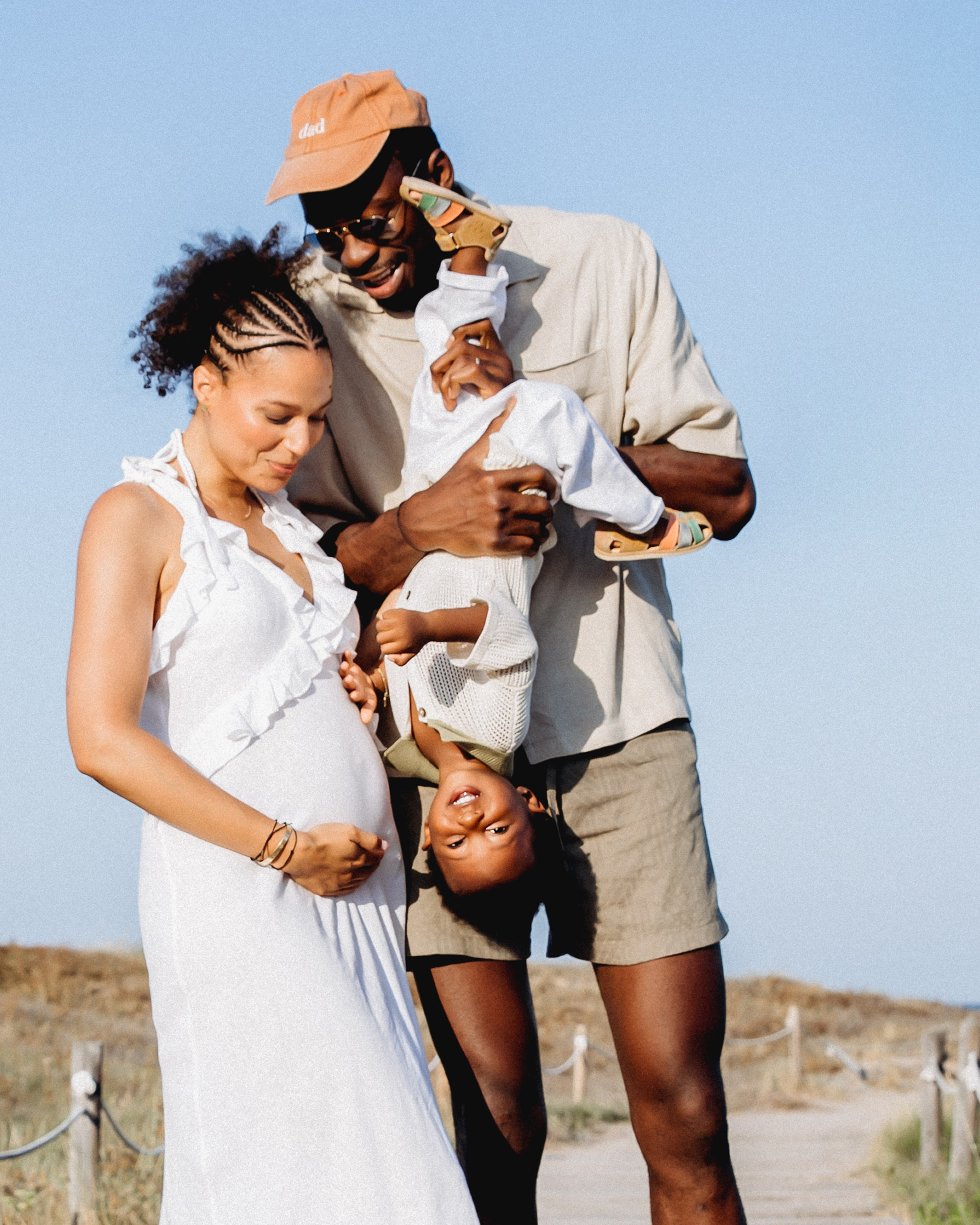 Sesión alegre de maternidad en Altea, España — familia riendo juntos en la playa, con la madre embarazada, el padre sonriente y su hijo disfrutando del momento. Inspiración ideal para fotografía de embarazo emocional y espontánea en la Costa Blanca.