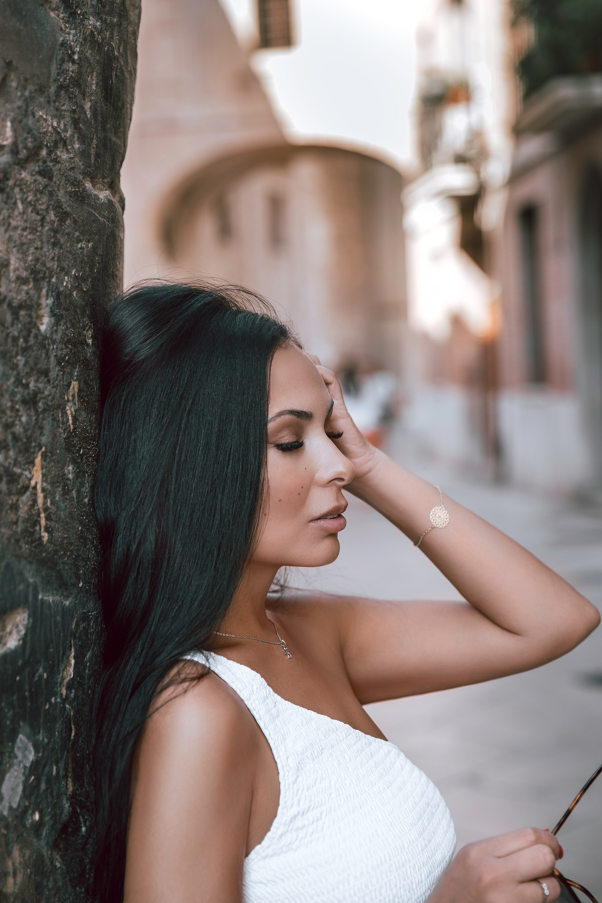 Женская фотосессия в Валенсии, Испания, с умиротворённым крупным портретом женщины, прислонённой к дереву на исторической улице, с мягким естественным светом, малой глубиной резкости и элегантной средиземноморской архитектурой на фоне — идеально для женской фотографии, портретных сессий, лайфстайл- и художественных съёмок, эмоциональных портретов и профессиональных женских фотосессий в Валенсии и по всей Испании.