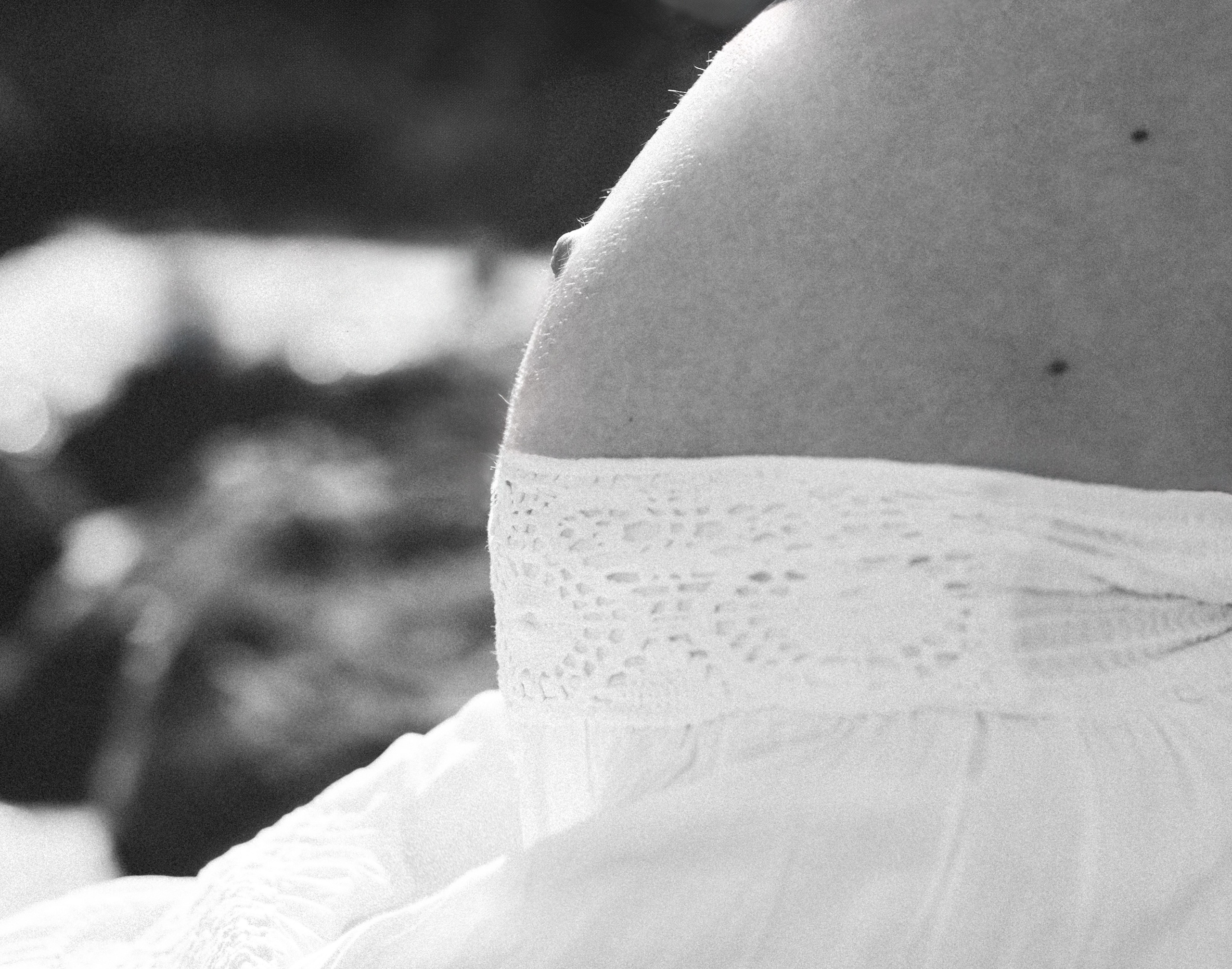 Sesión de fotos de embarazo en blanco y negro en València, España, con un primer plano íntimo de la barriga de una mujer embarazada envuelta en una delicada tela blanca, capturada con luz natural suave y una atmósfera minimalista y emocional — ideal para fotografía de embarazo, sesiones de maternity, retratos artísticos de embarazo, sesiones íntimas de embarazo y sesiones románticas de maternity en València y en toda España.