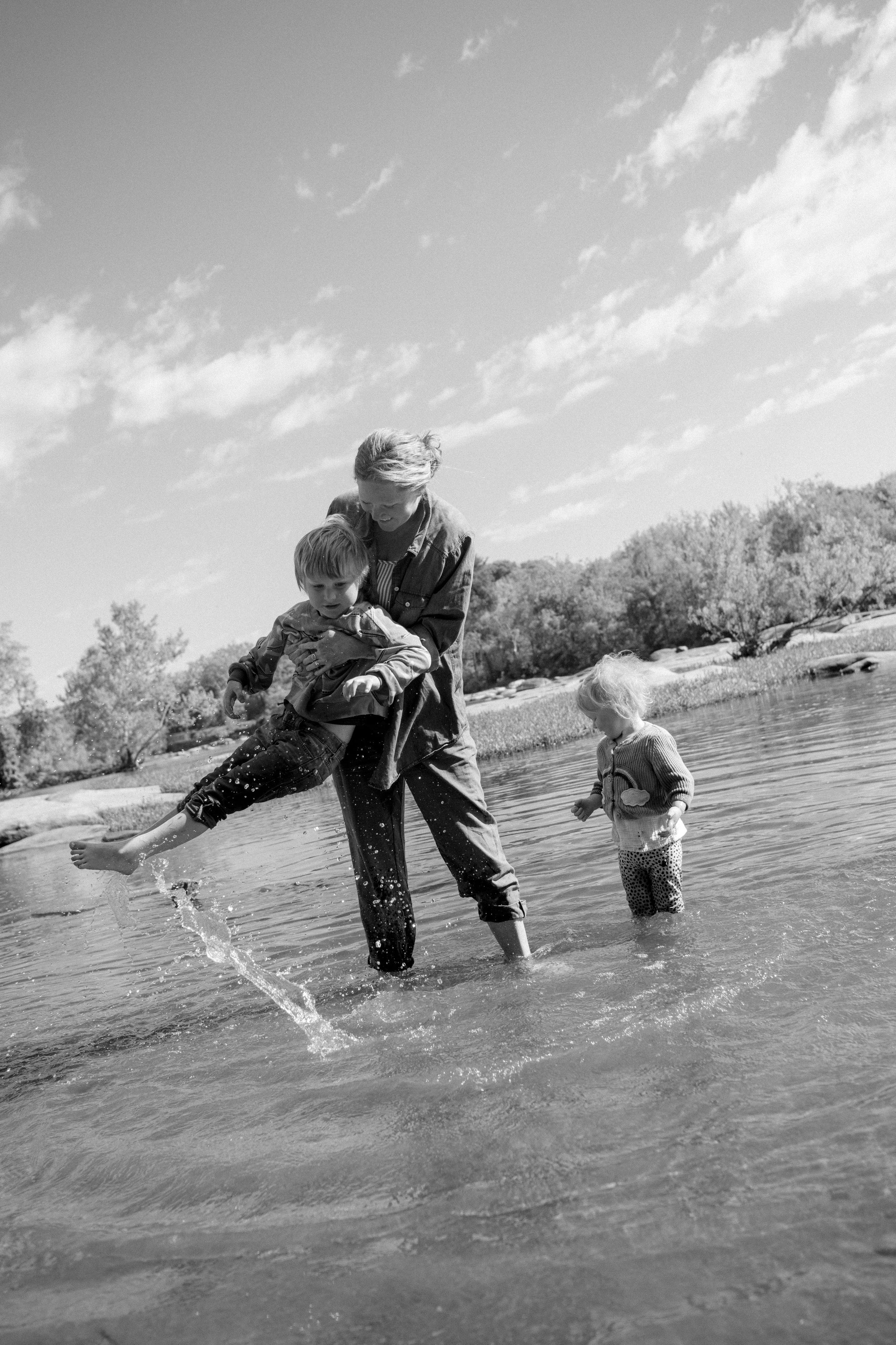 Children and their mom splashing and playing in the warm river water during a summer family photo session at Pony Pasture