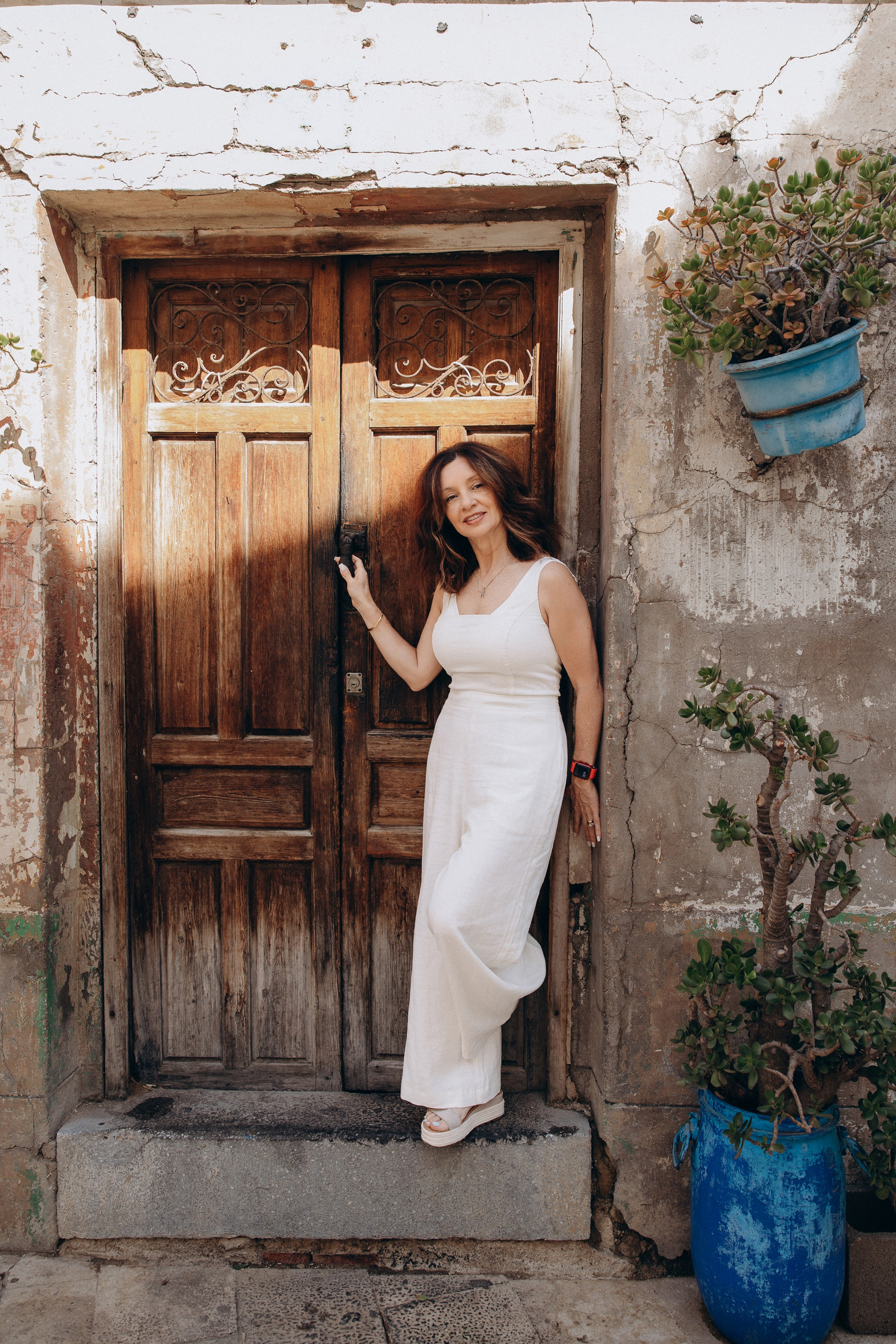 Women’s portrait photoshoot in Valencia, Spain featuring a woman in an elegant white dress posing beside a rustic wooden doorway. Lifestyle portrait ideal for women’s photography, solo photoshoots, vacation portraits and professional portrait photography in Valencia and Spain.
