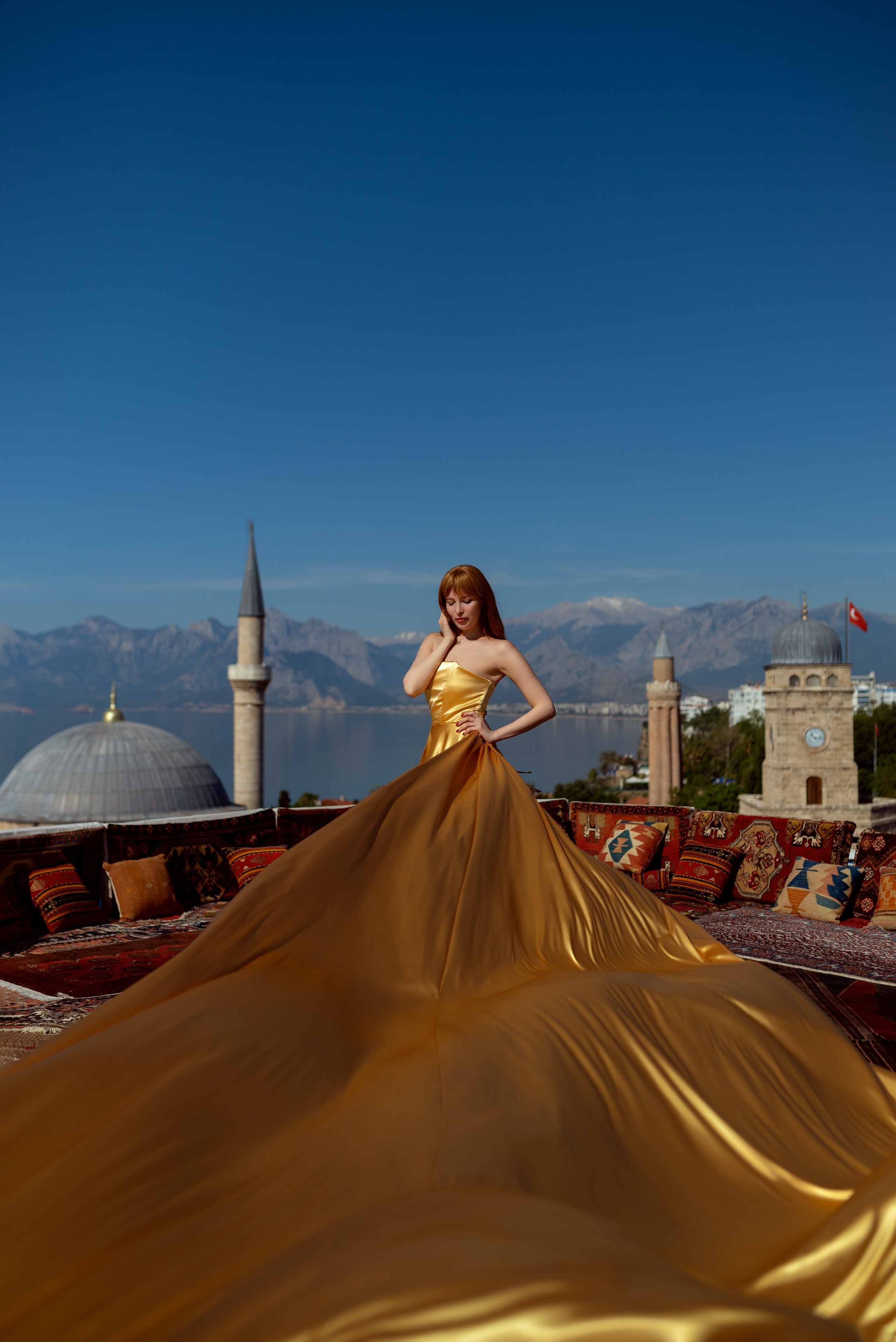 Девушка в платье со шлейфом на крыше с коврами с видом на достопримечательности