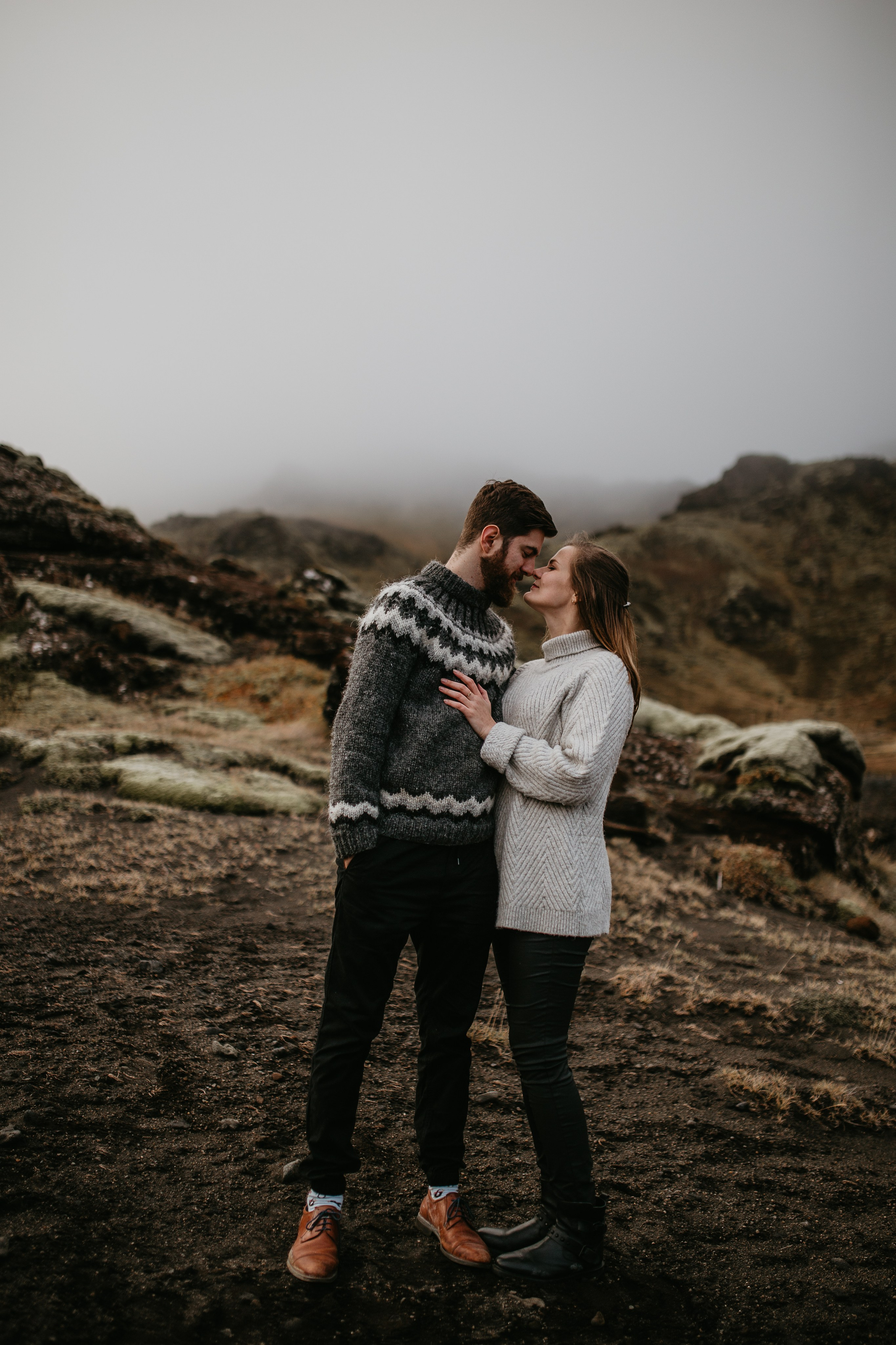Adventurous couple standing on a black sand beach in Iceland, with dramatic cliffs in the background.