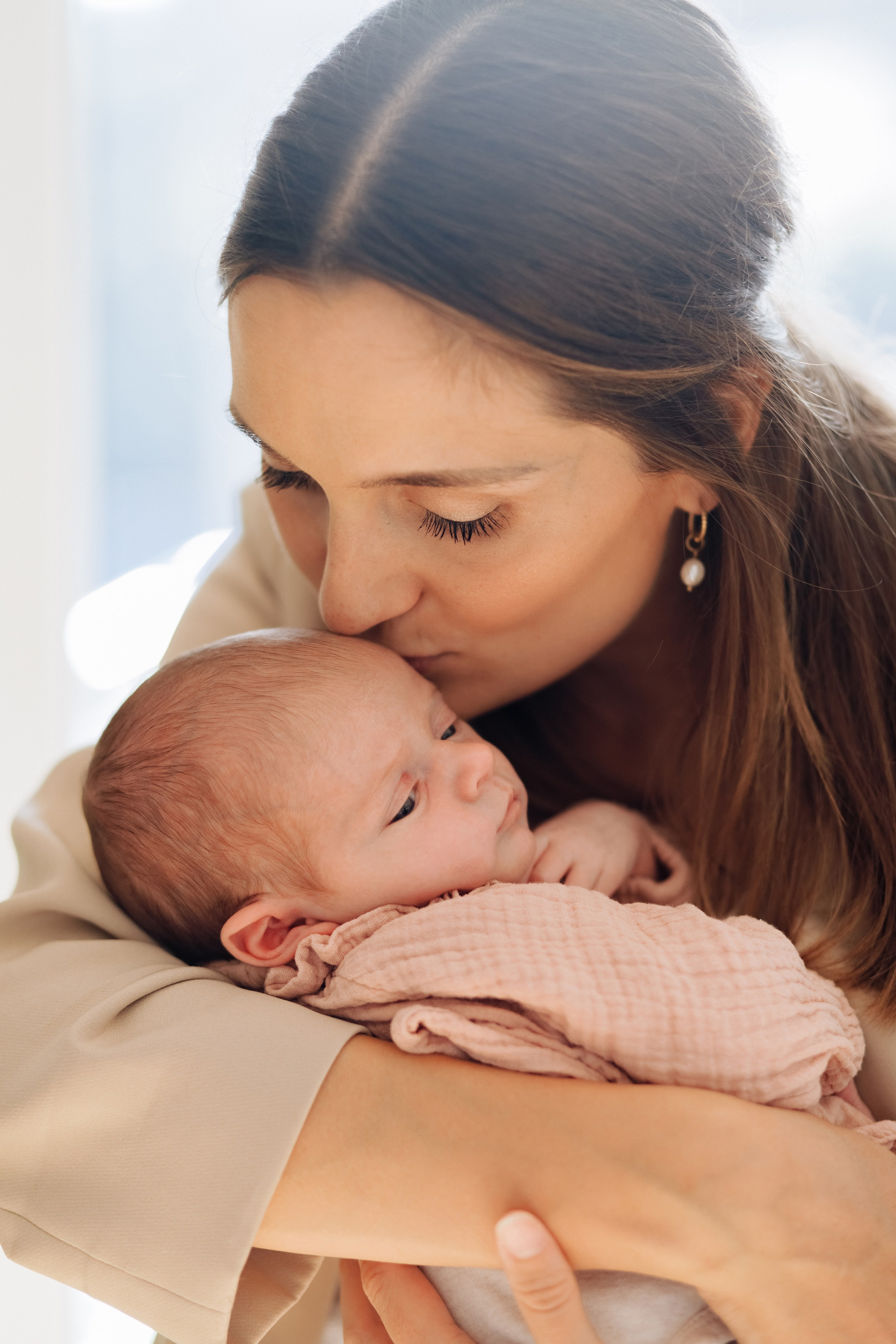 Mutter küsst ihr Baby in einem hell erleuchteten Raum.