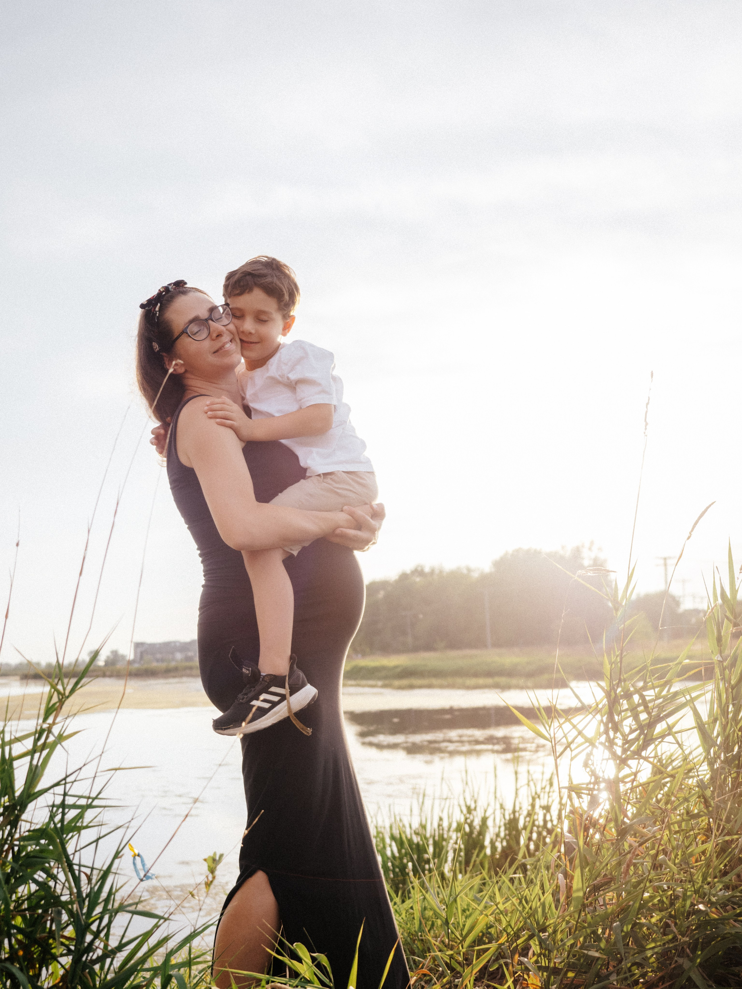 Pregnant woman holding her son in an outdoor setting with sunset light.