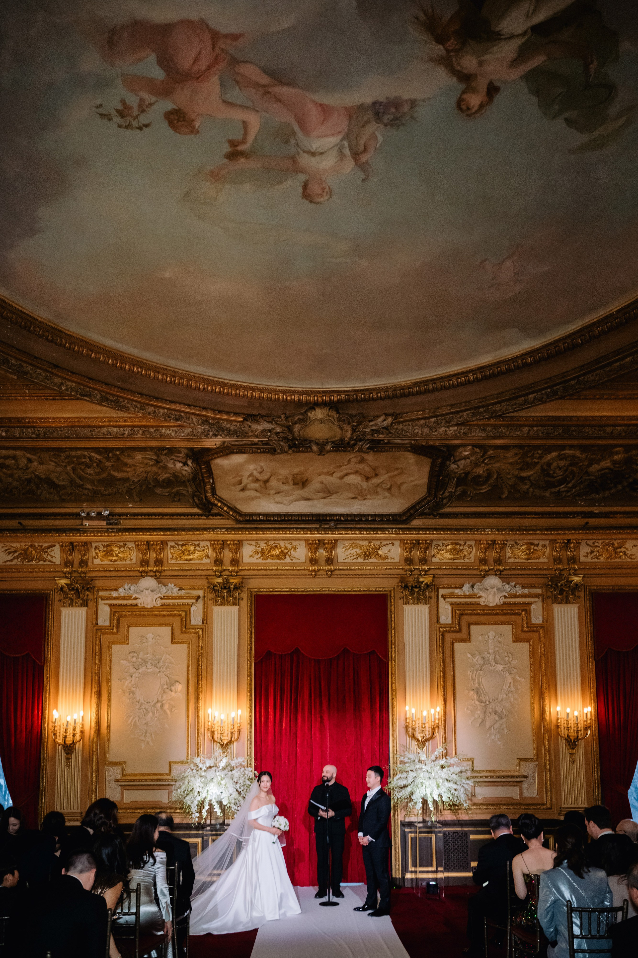 a bride and groom are standing in front of a red curtain