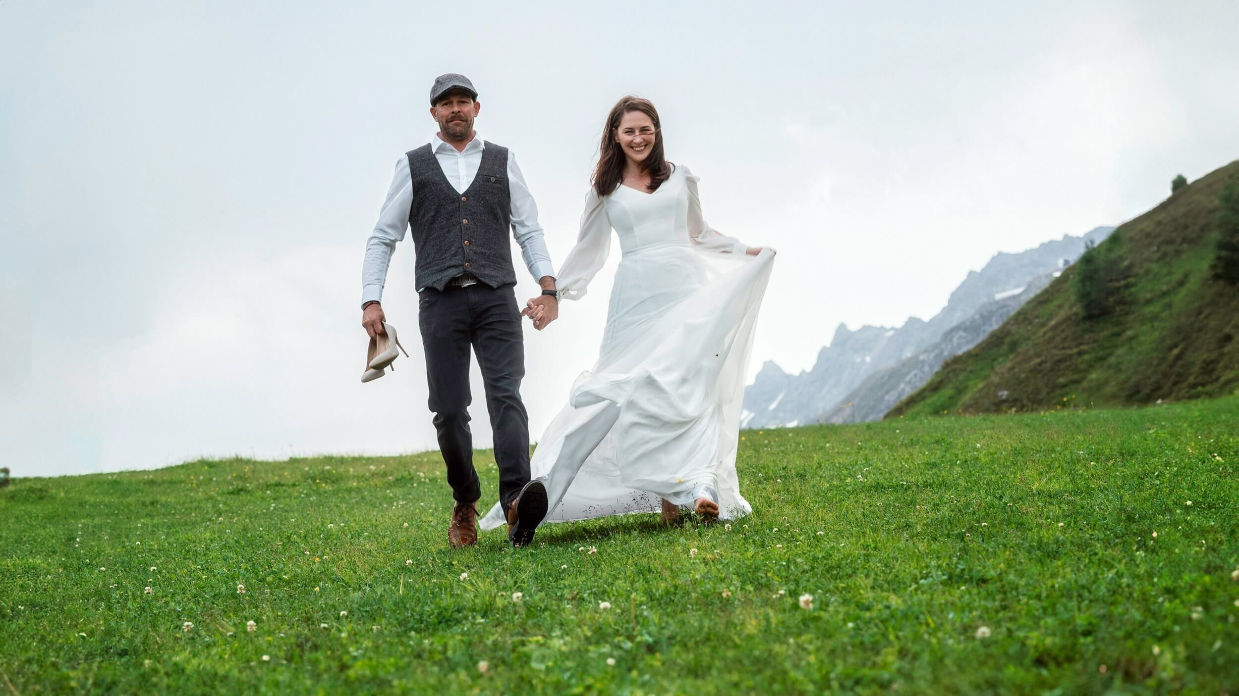 Hochzeitsfotograf in Sölden fängt den Moment ein: Paar läuft Hand in Hand mit Bergblick. 