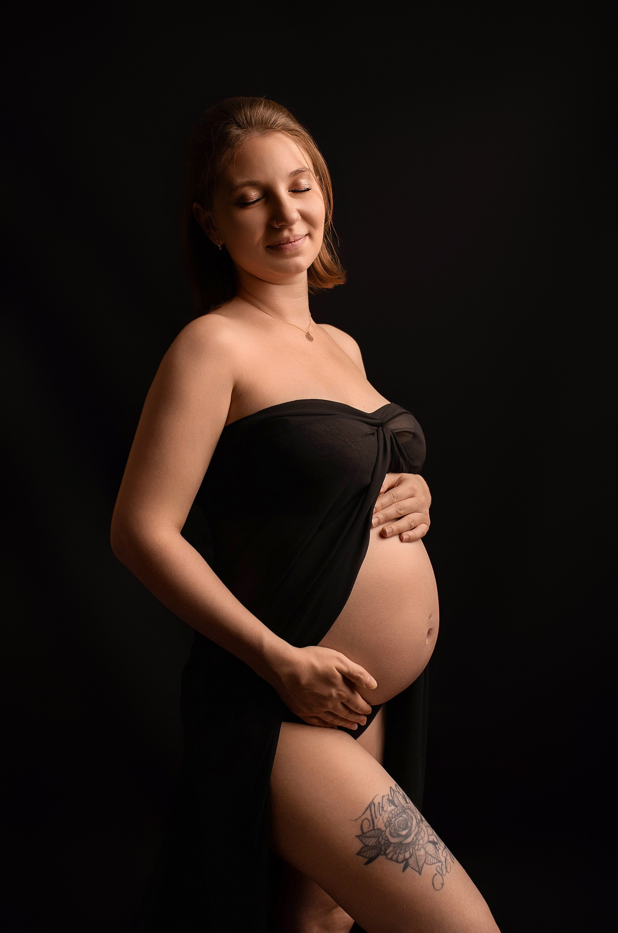 werdende Mama in schwarzem Tüll hält Babybauch und hat die Augen geschlossen - Schwangerschaftsfotografie Weißenhorn bei Ulm