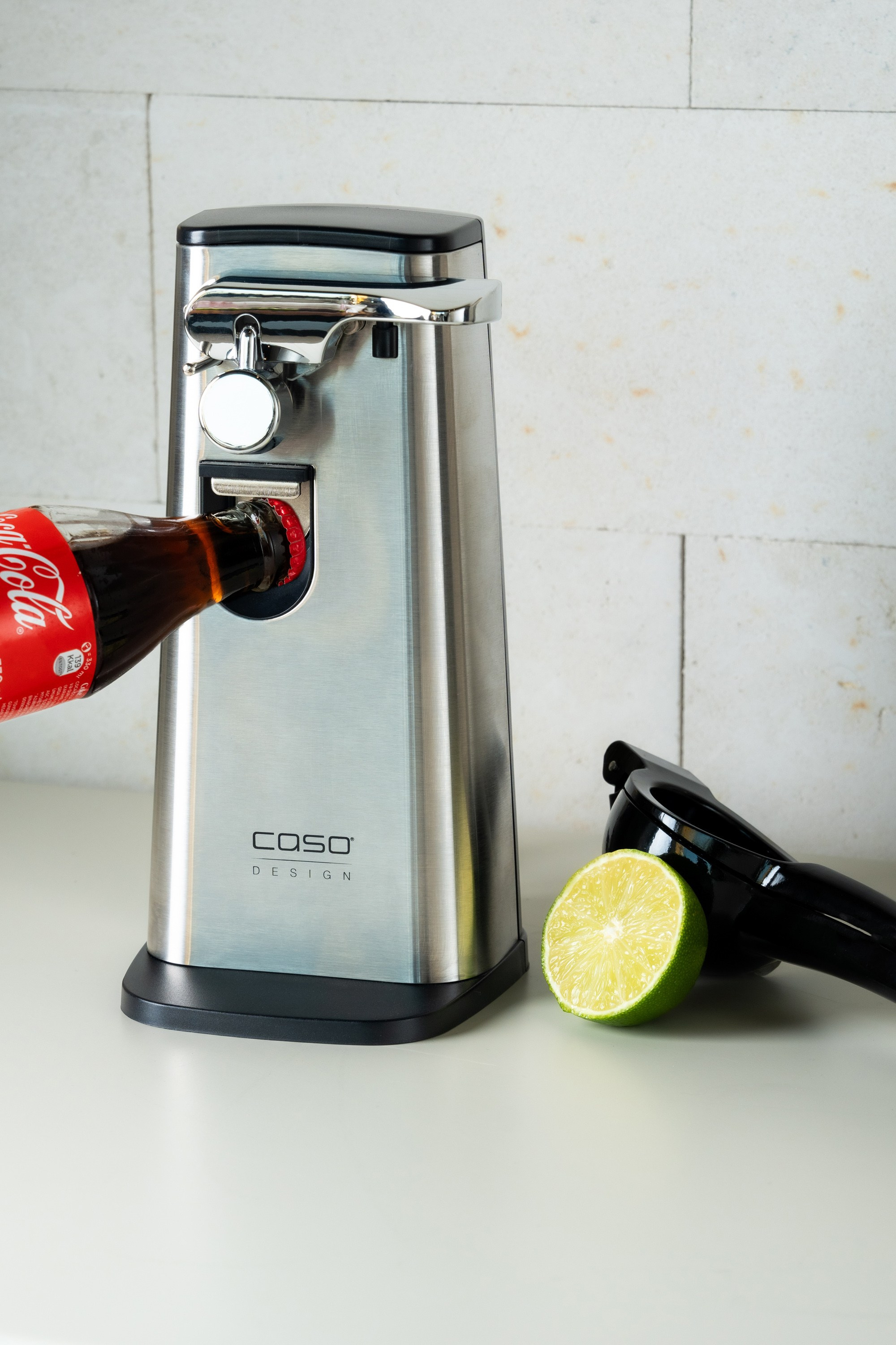 Caso Design elektrik butulka açarı, Coca-Cola şüşəsi və limon ilə ağ fon qarşısında məhsul çəkilişi.