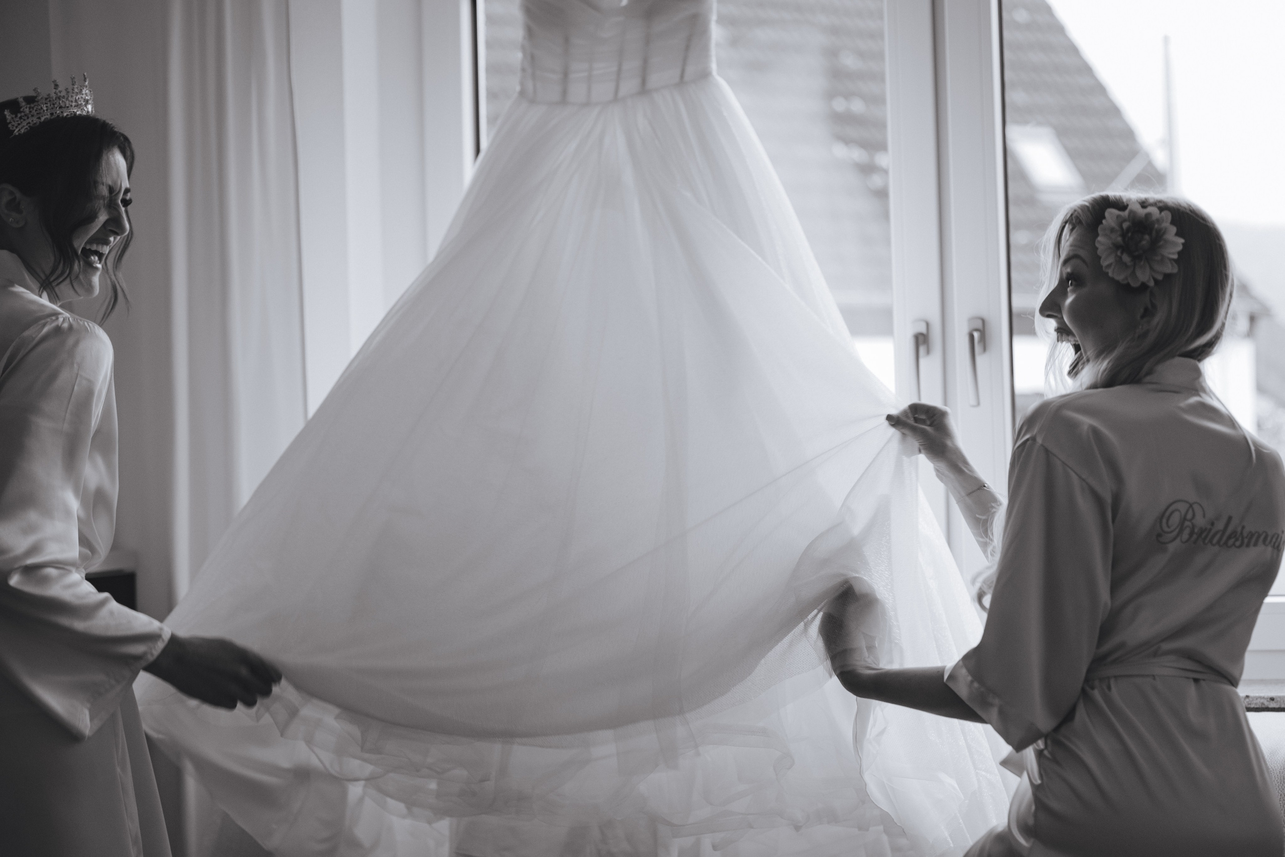 Die Braut und ihre Trauzeugin lachen und schütteln den Tüll des Hochzeitskleides. Schwarz-Weiß-Foto eines fröhlichen Moments.