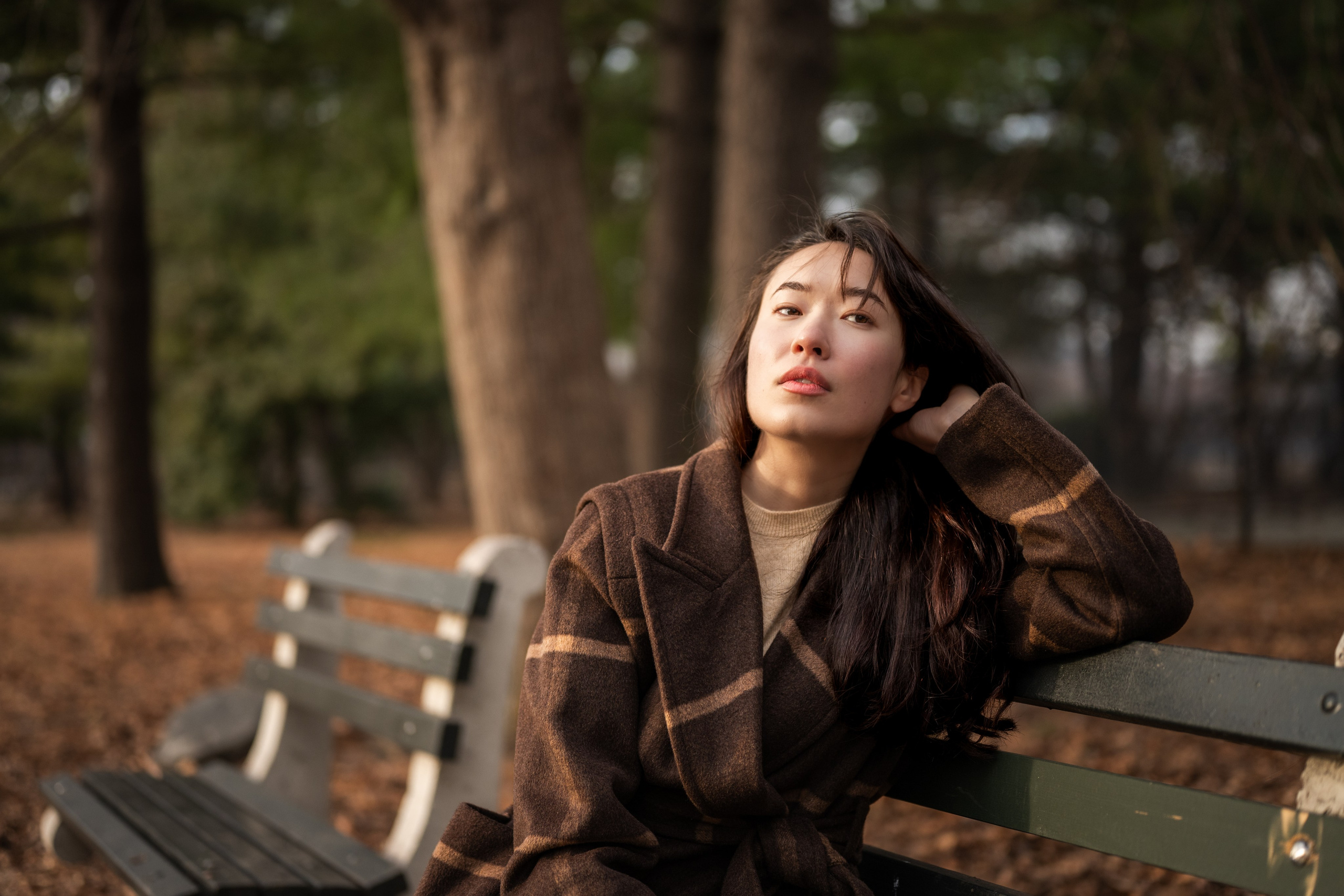 Woman relaxing on a park bench in Van Cortlandt Park, Bronx, New York, lifestyle portrait with soft background blur.