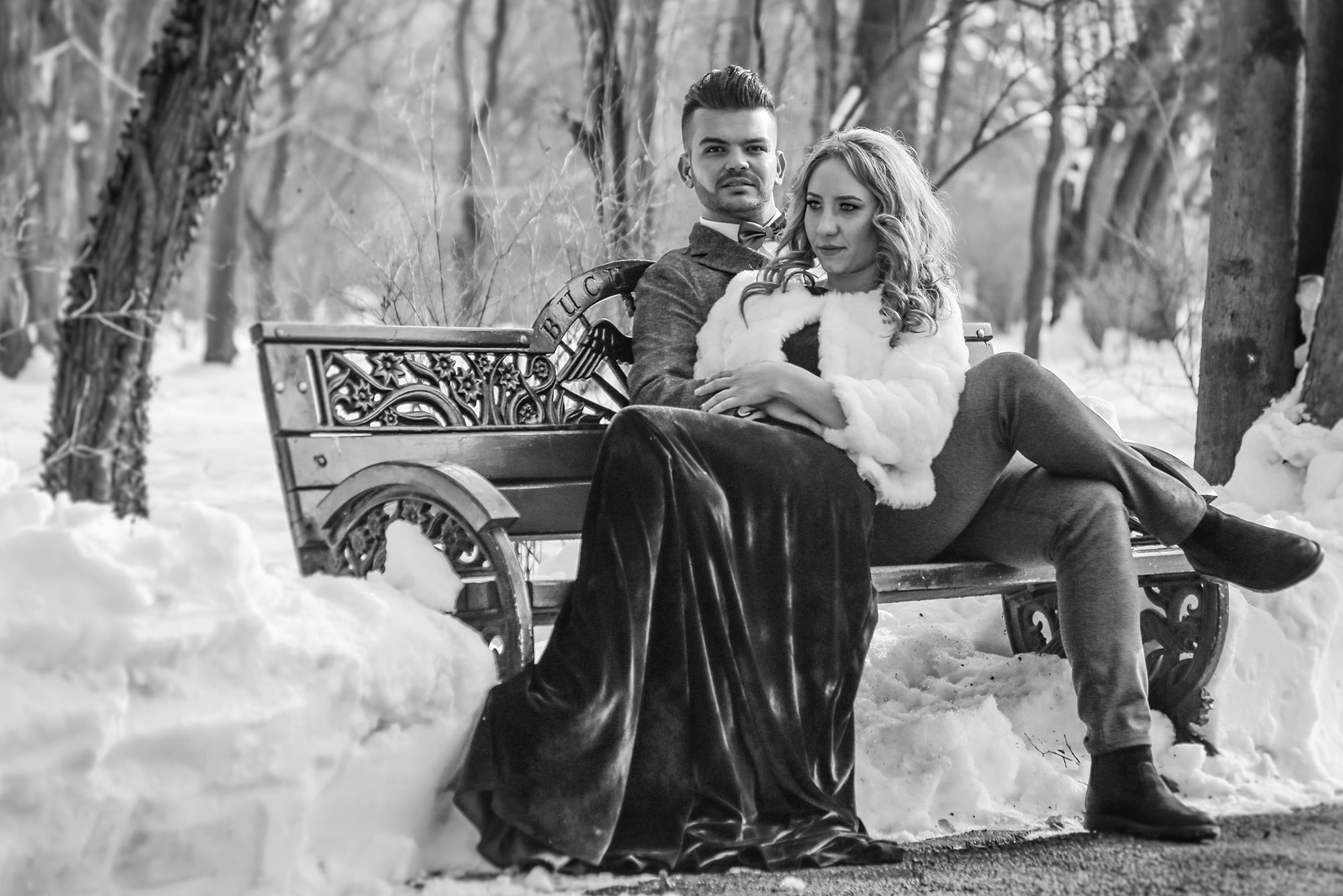 Black and white wedding photo of the bride and groom sitting on a snow-covered park bench, creating a nostalgic winter vibe.