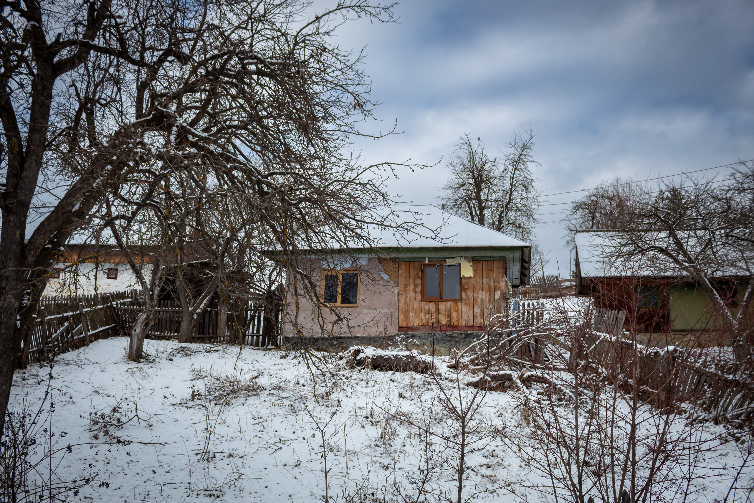 Traditional village house surrounded by trees and deep snow in a rural winter scene.
