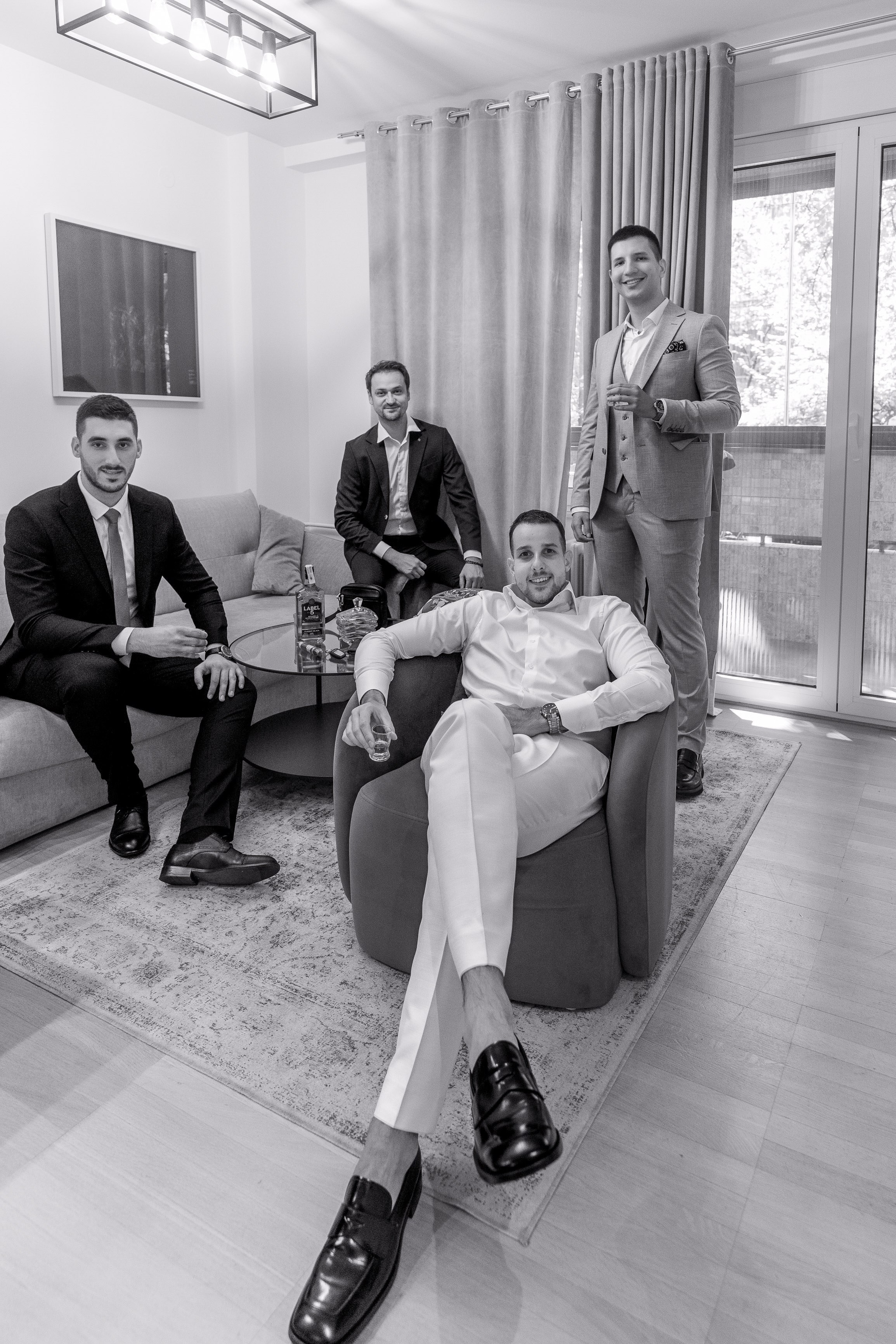 mladozenja sedi u fotoelji i oko njega su tri muskarca