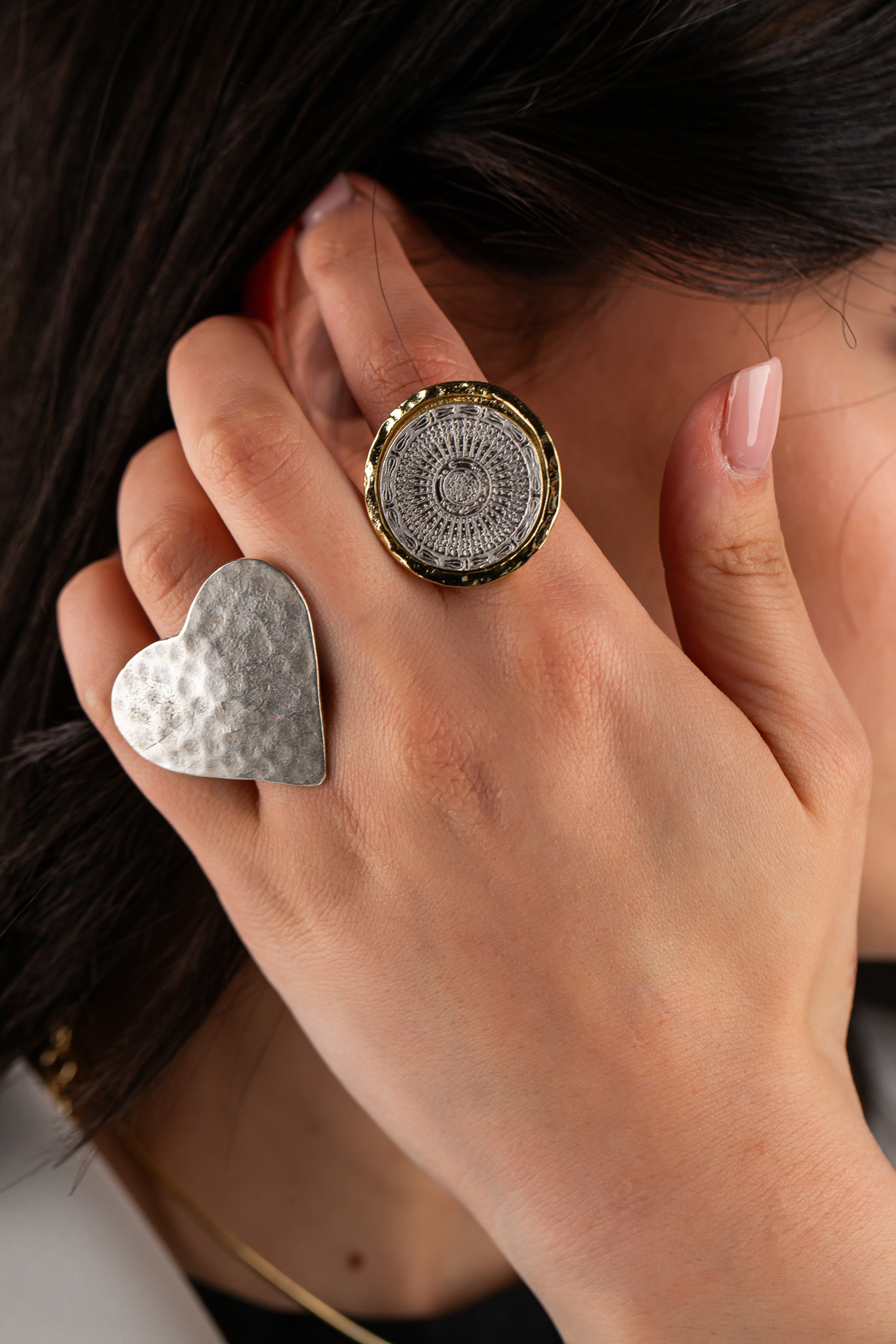 İki böyük üzüklü əlin yaxından görünüşü: döyülmüş gümüş ürək və yuvarlaq, toxumalı qızıl və gümüş üzük.