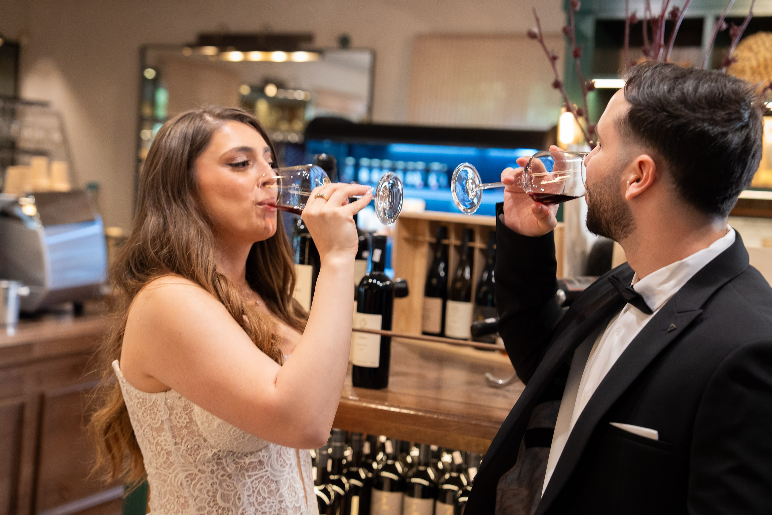 Bride Tzipi and groom Ron drinking red wine during their wedding photoshoot at Amphora Winery, Israel
