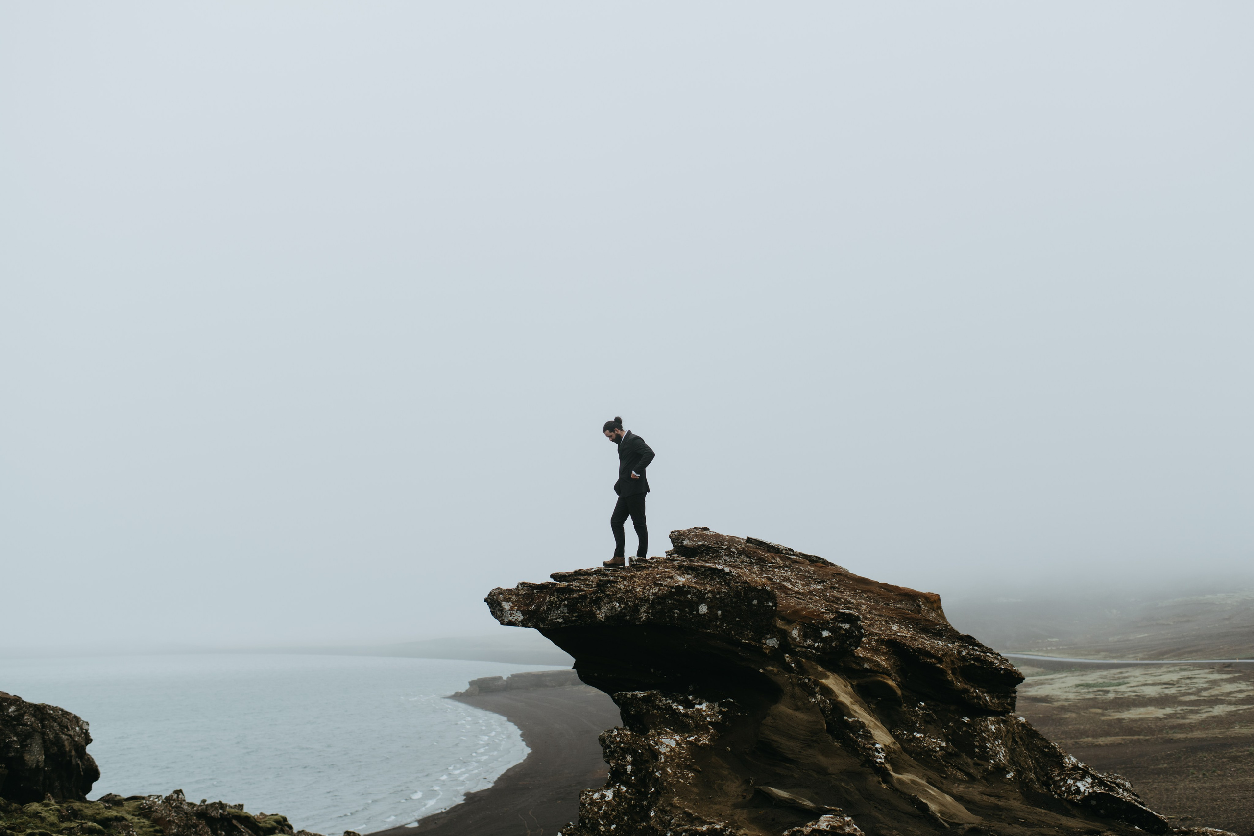 Bride and groom looking out over the vast, mysterious waters of Kleifarvatn, their wedding outfits contrasting against the dark landscape.