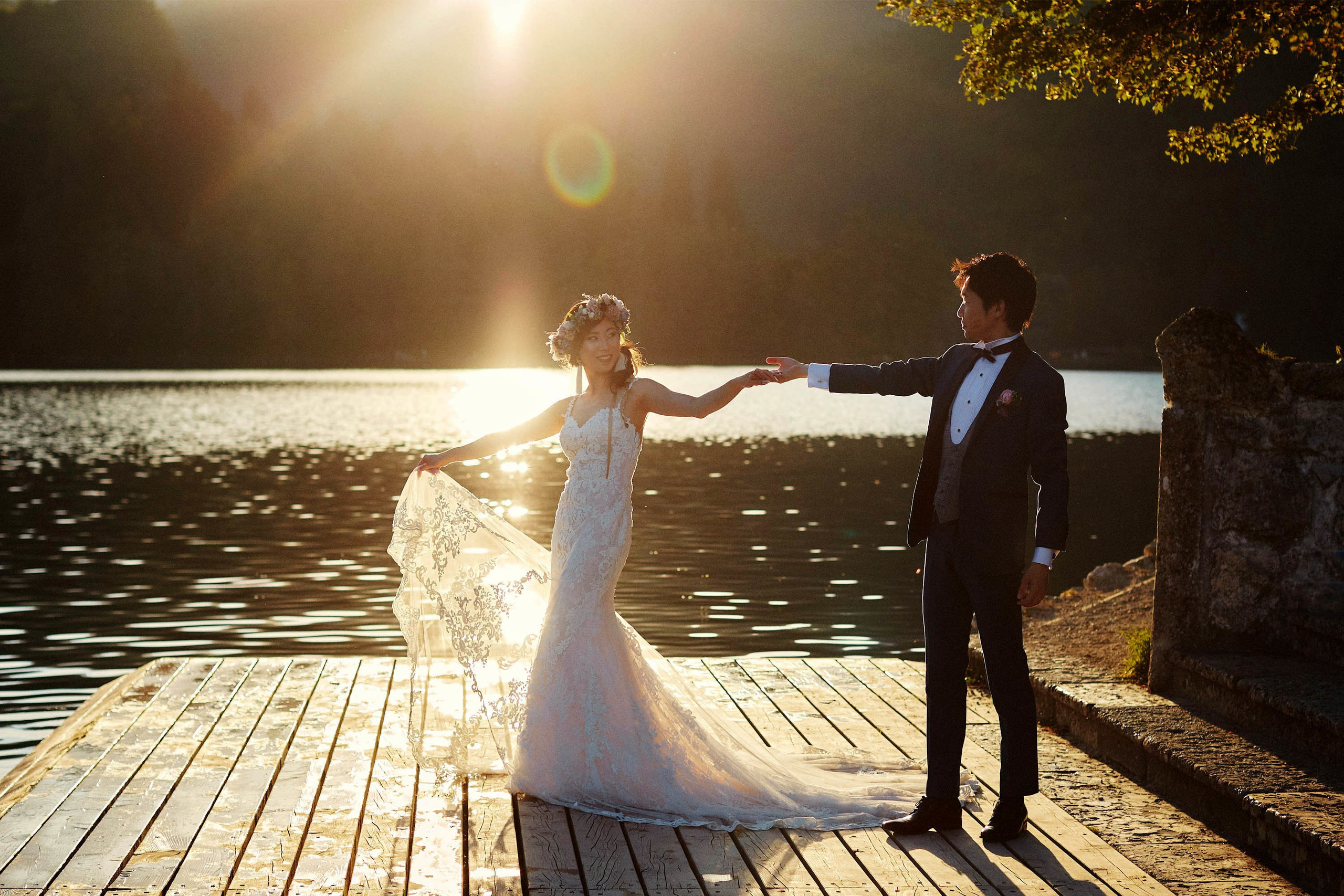 Groom leading bride hand-in-hand golden hour Lake Bled dock.