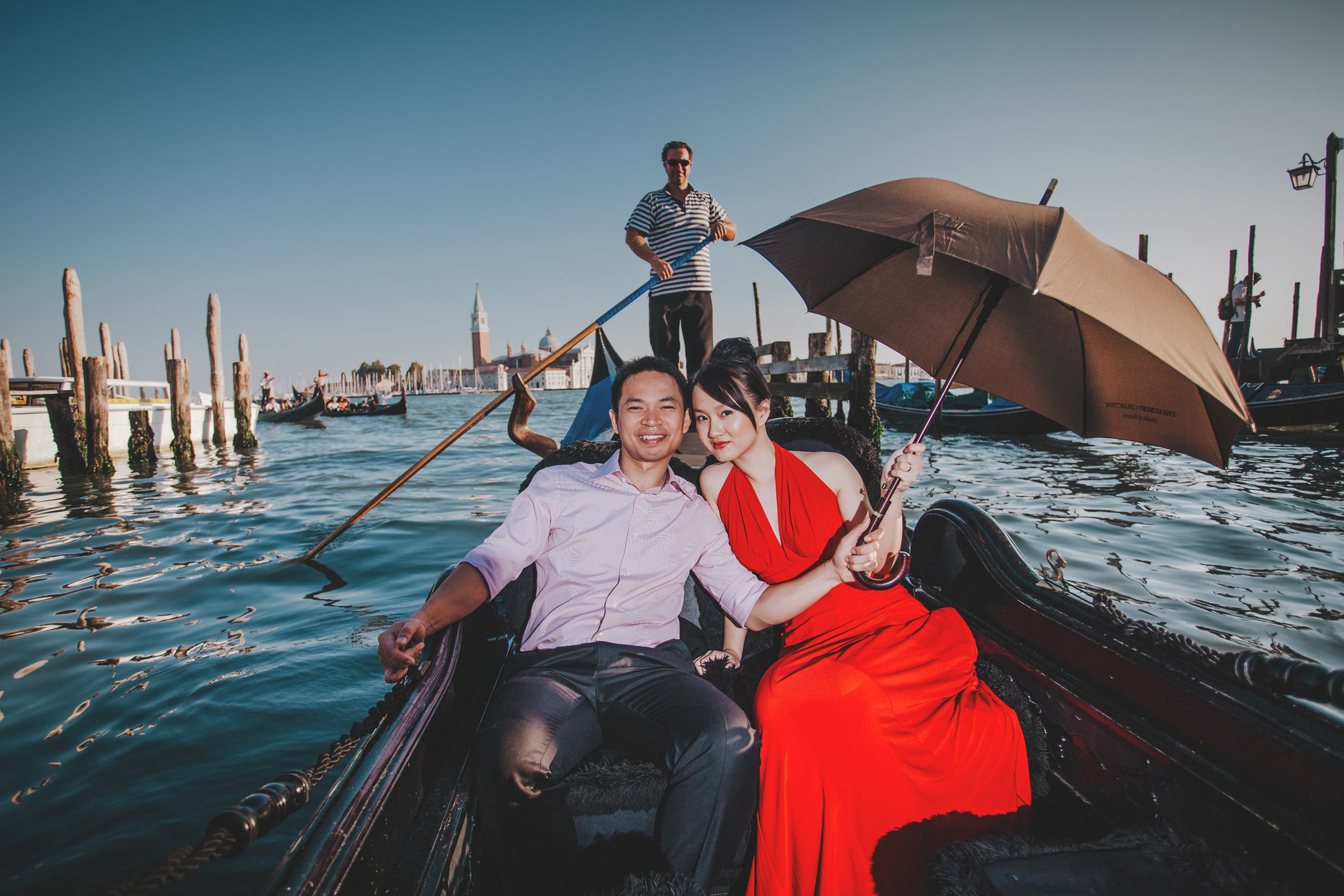 Smiling Thai man holding umbrella over fiancee during gondola ride in Venice canals.