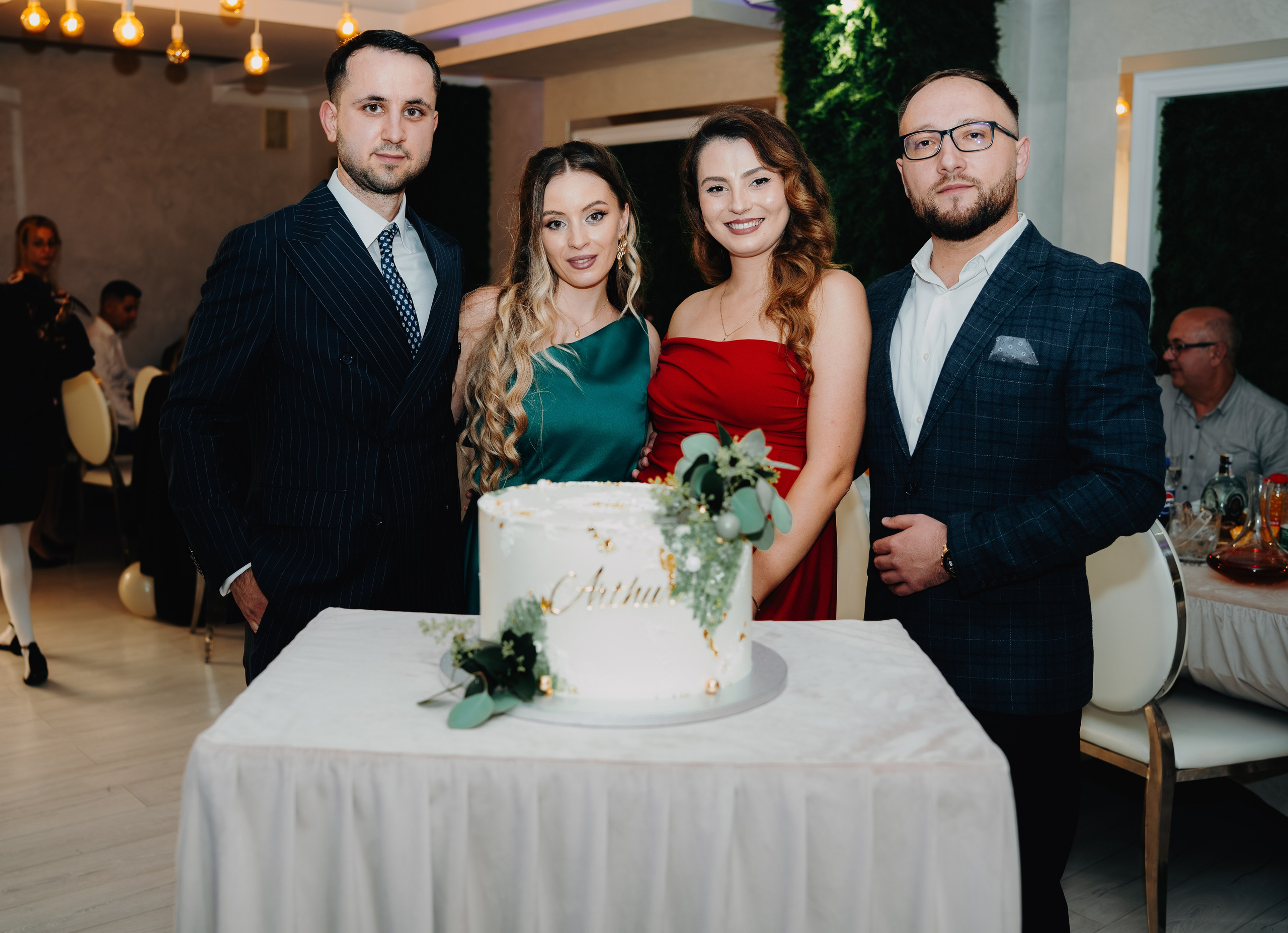 Momentul simbolic al tăierii tortului la botezul lui Arthur Mihail la Restaurantul Monden din Bârlad. Părinții și nașii sunt grupați în jurul tortului decorat, pregătindu-se să taie primul felie sau să ridice un toast, într-o poză de unitate și bucurie comună.