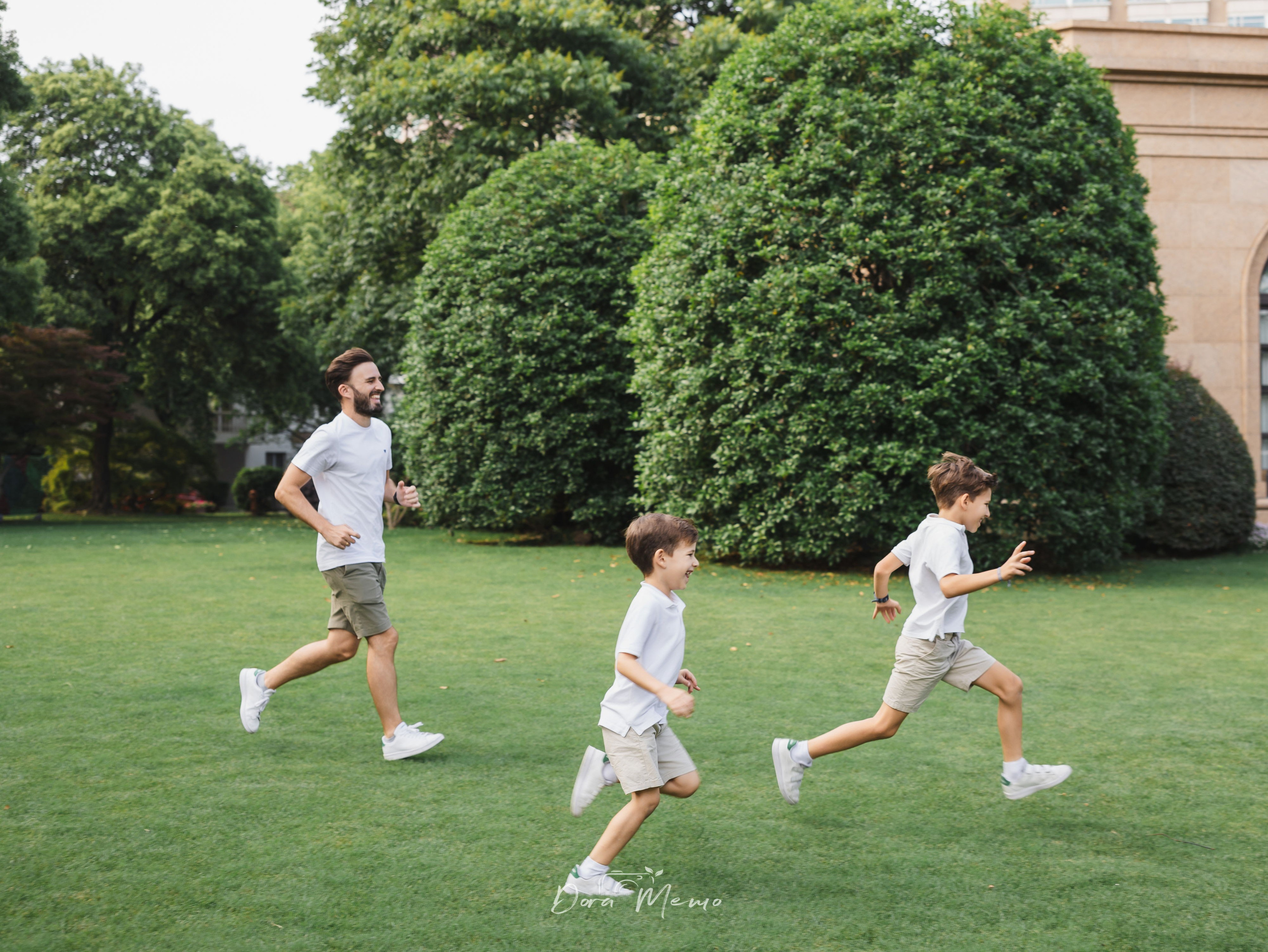 Dad running with two boys on the grass | Father running with his sons across a sunlit lawn, full of energy 