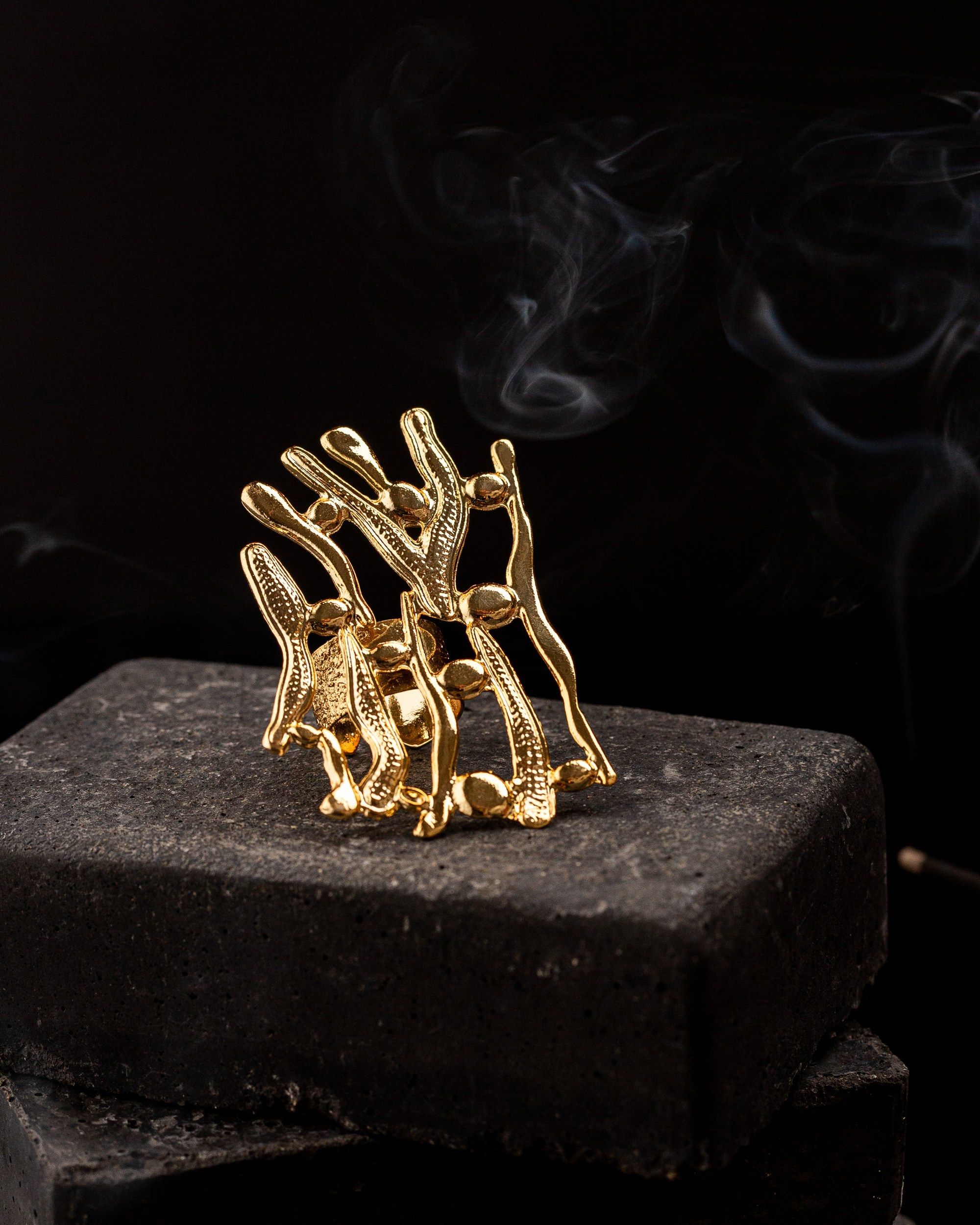 Arxa planda tüstü lələyi ilə tünd daş üzərində nümayiş etdirilən, teksturalı səthə malik müasir, abstrakt qızılı rəngli üzük.