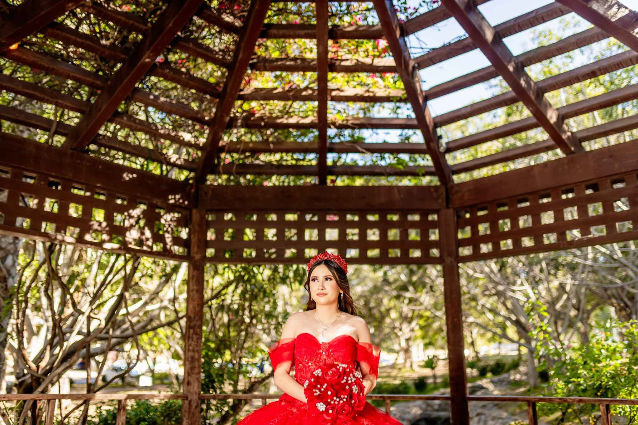Quinceanera bajo estructura de madera en Parque Hacienda Aguacaliente Tijuana vestido rojo fotografia profesional en exterior