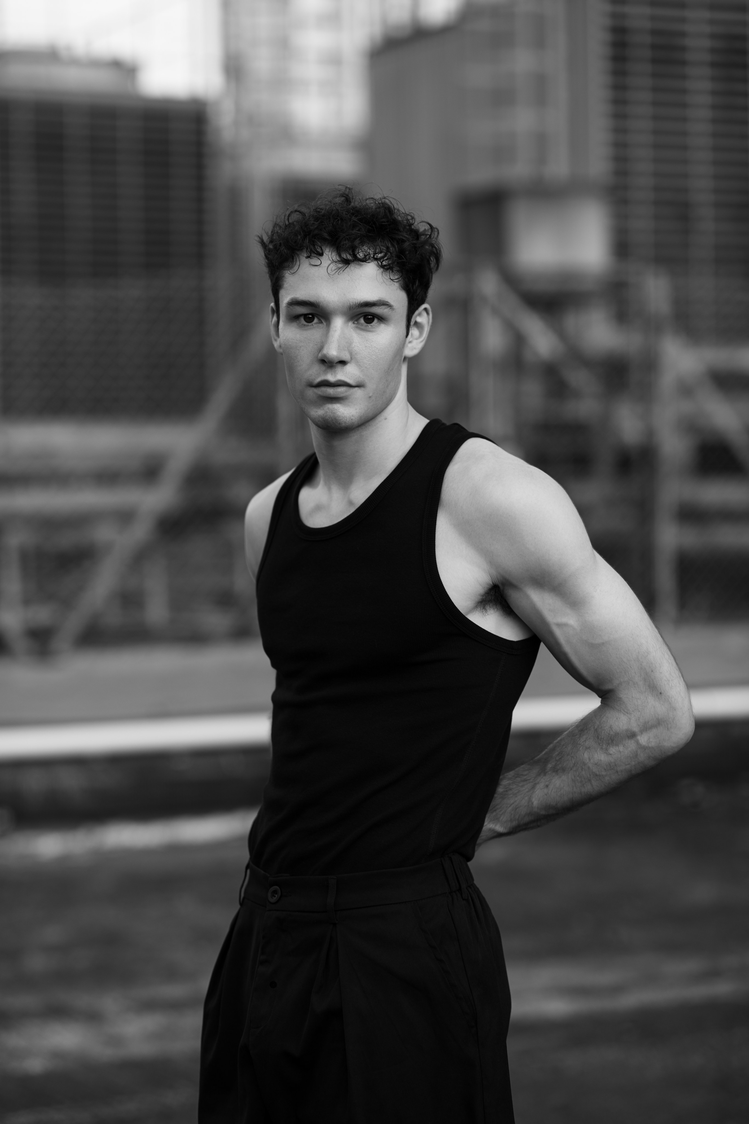 Standing profile of a male model on a downtown Singapore rooftop, CBD high-rises soft in the distance.