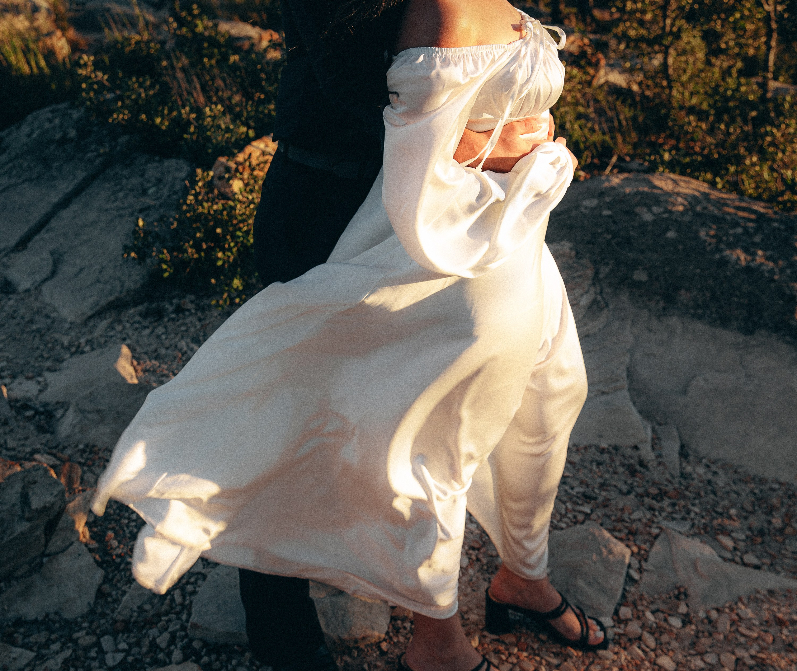 Engagement photoshoot in València, Spain, capturing an intimate moment of a couple embracing on rocky mountain terrain, with the bride’s flowing white dress moving in the warm golden-hour light — a romantic and artistic engagement and wedding love story image ideal for engagement photography, pre-wedding sessions, elopements, and professional wedding photoshoots in València and across Spain.