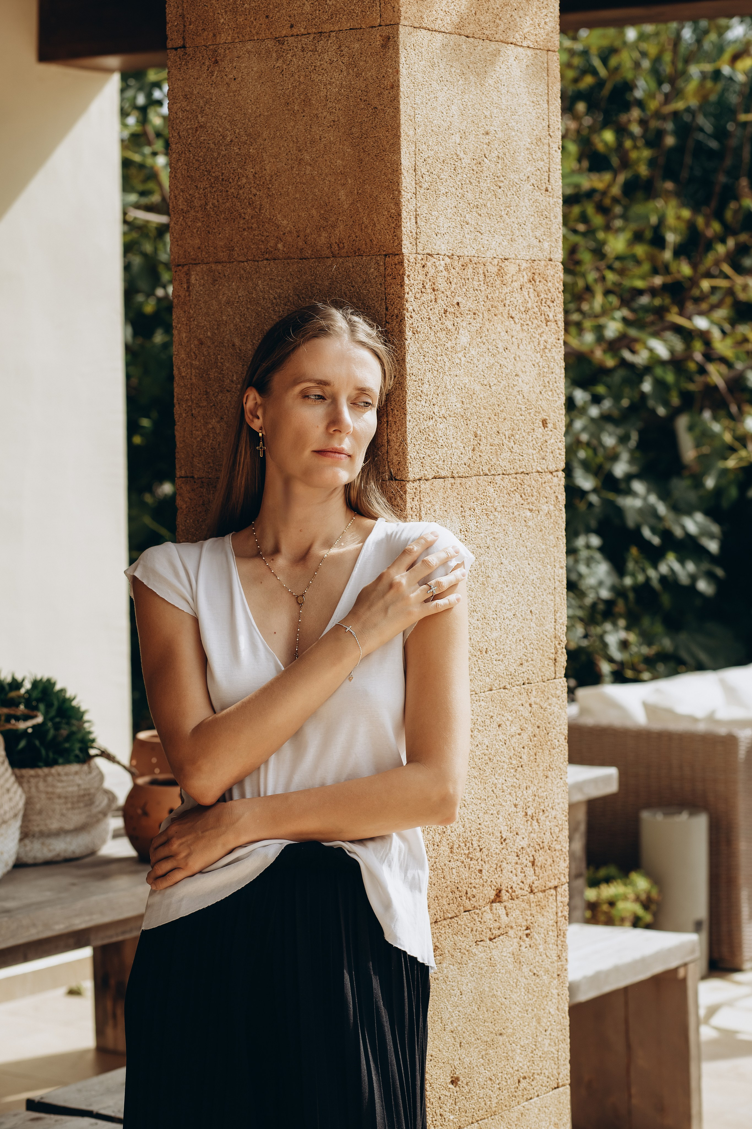 Stylish brand photoshoot in Valencia, Spain featuring a woman posing in natural light against a stone column, showcasing minimalist fashion and jewelry. Perfect for fashion, content, and lifestyle brands seeking product photography in Valencia or across Spain.