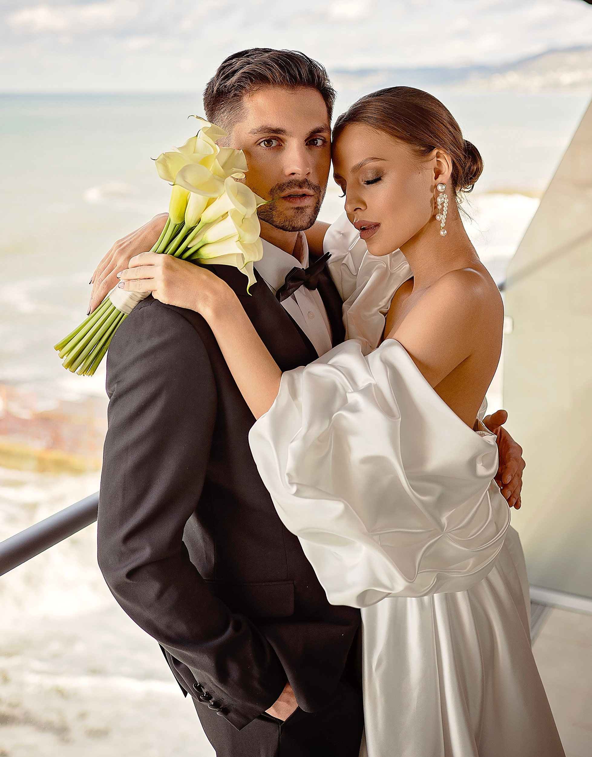 Bride and groom embracing by the coast with a calla lily bouquet. Outdoor destination wedding photographer in Munster, Ireland