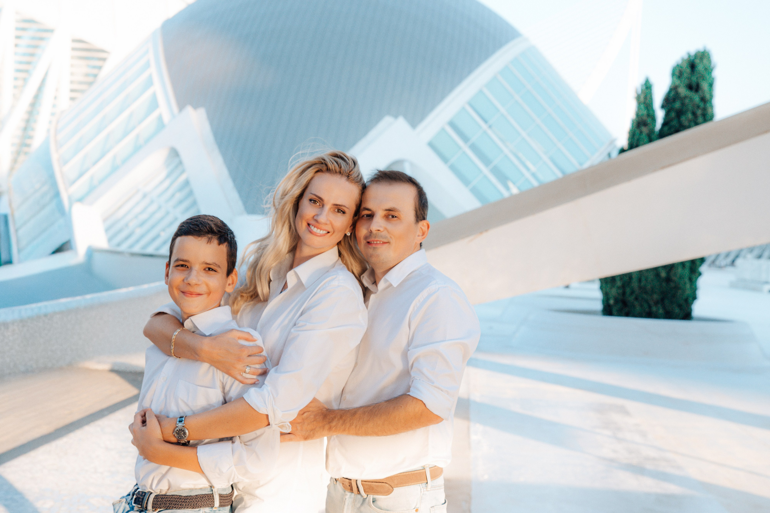 Familia sonriente posando frente a la arquitectura futurista de la Ciudad de las Artes y las Ciencias en Valencia, España. Este retrato familiar moderno y elegante es perfecto para quienes buscan sesiones familiares memorables en Valencia y en toda España.