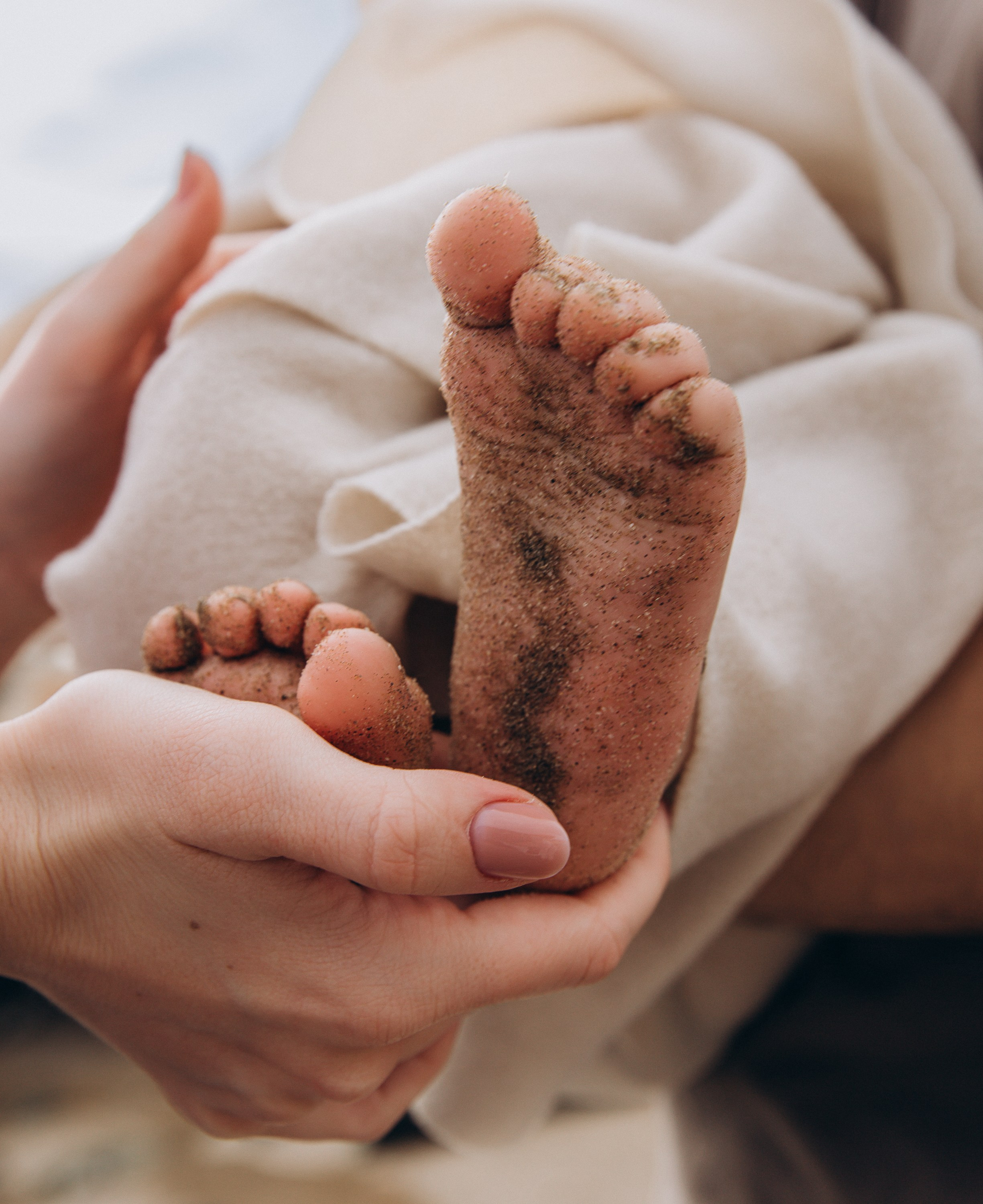 Primer plano de los pies arenosos de un bebé sostenidos con ternura por las manos de un padre durante una emotiva sesión de fotos familiar en la playa de Valencia, España. Esta imagen natural y emotiva captura la esencia del amor y la conexión — perfecta para quienes buscan sesiones familiares auténticas en Valencia y en toda España.