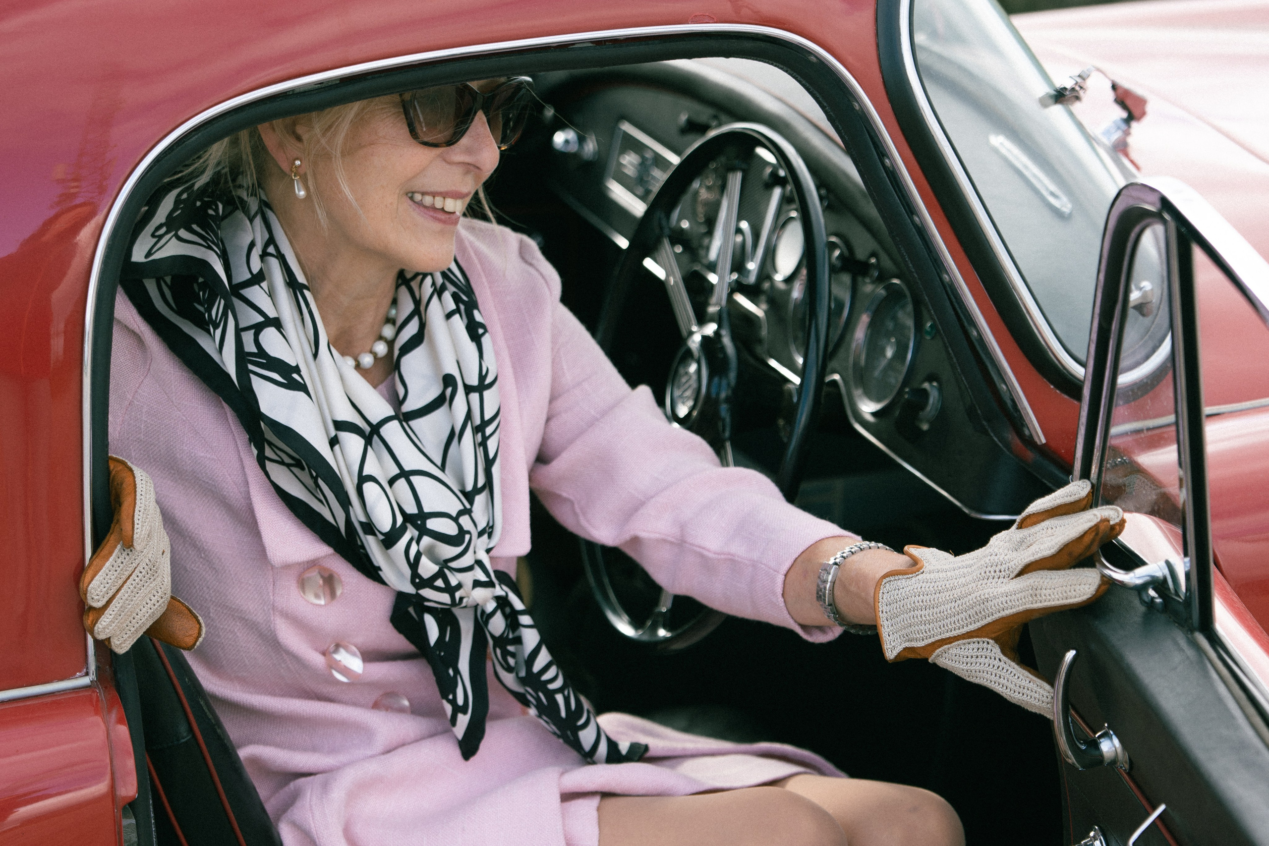 Editorial portrait of a woman in a pink suit with a classic red sports car