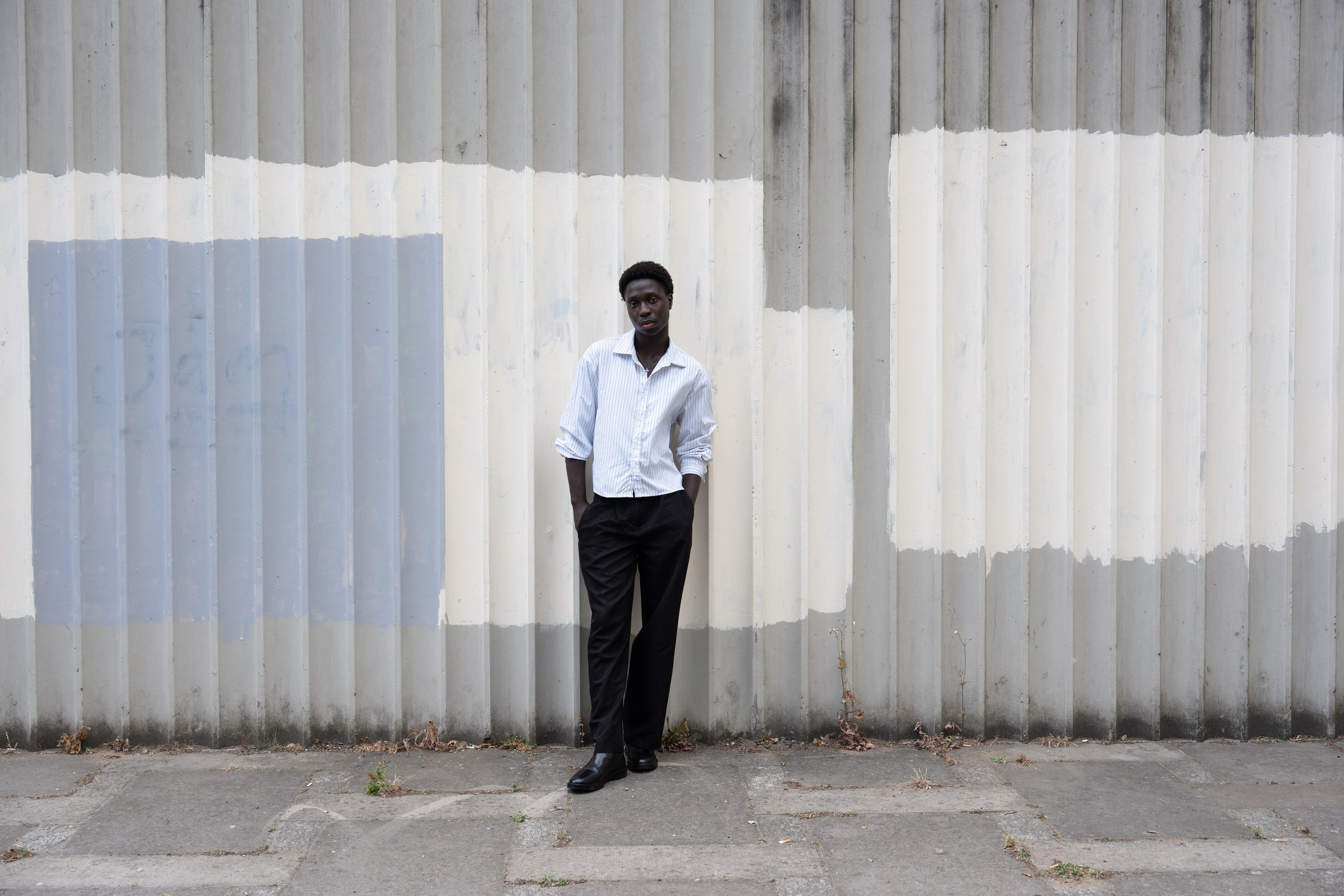 Editorial fashion portrait of a male model against a striped industrial wall