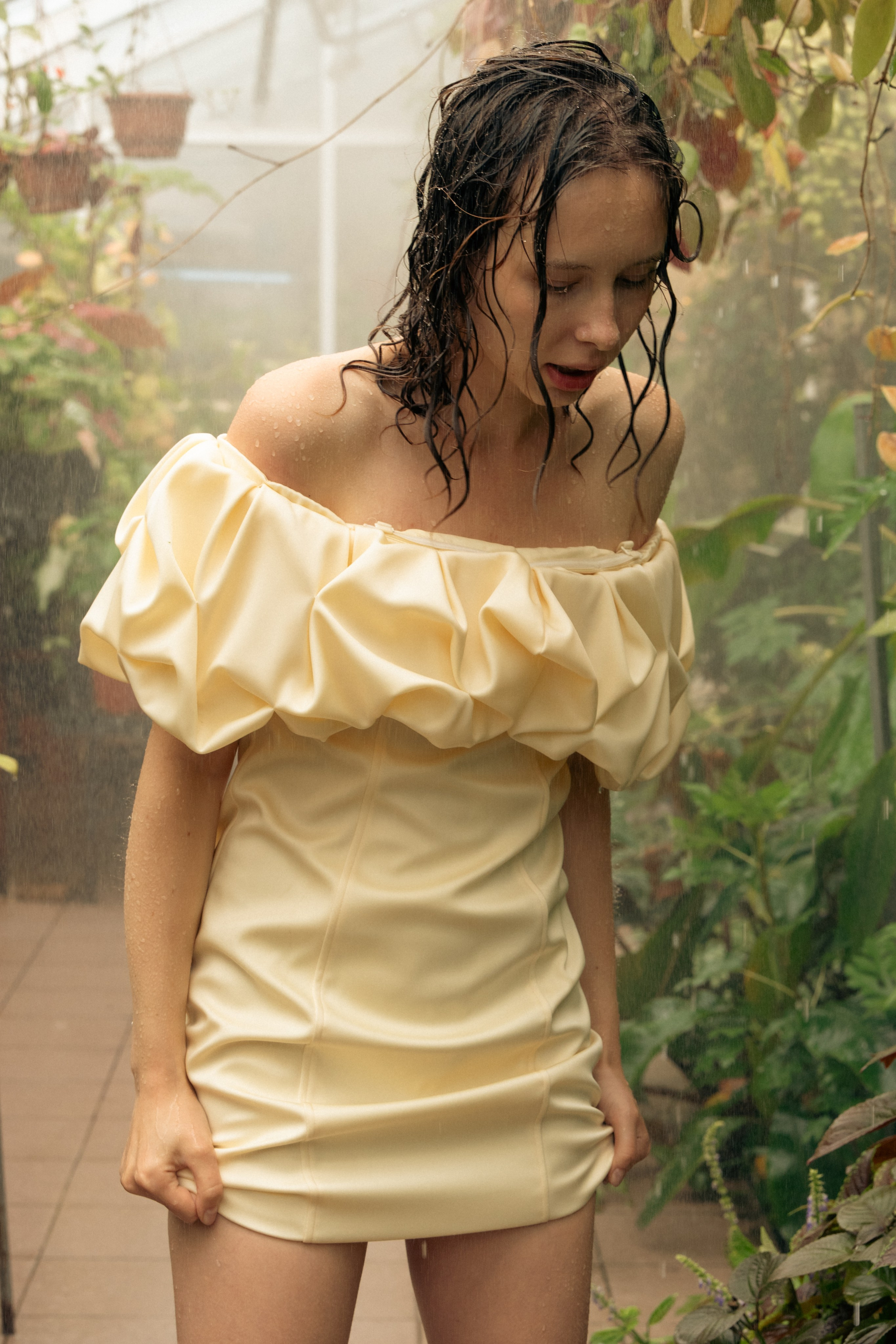 Fashion portrait of a woman with wet hair in a cream dress in a greenhouse