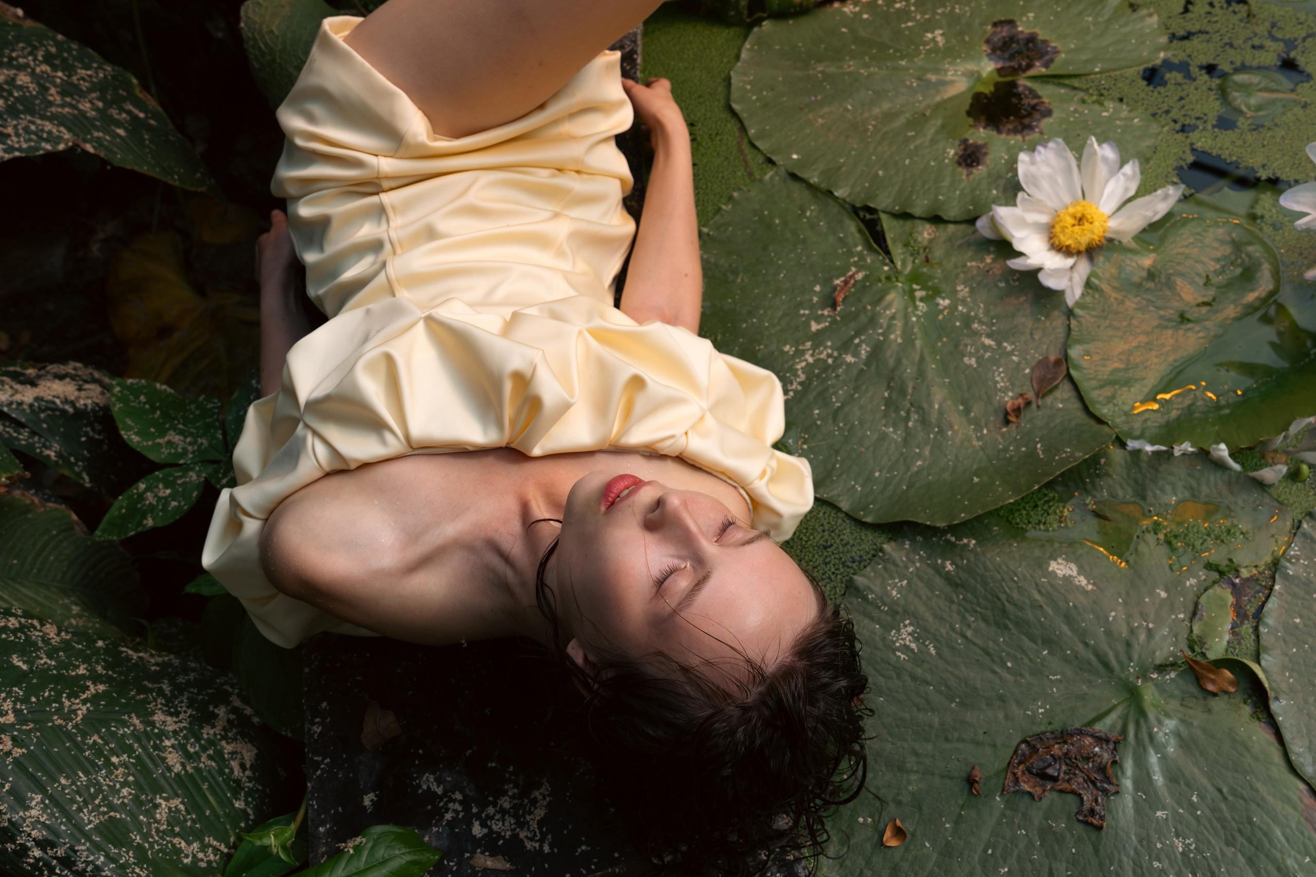 Editorial fashion portrait of a woman in a cream dress beside a lily pond