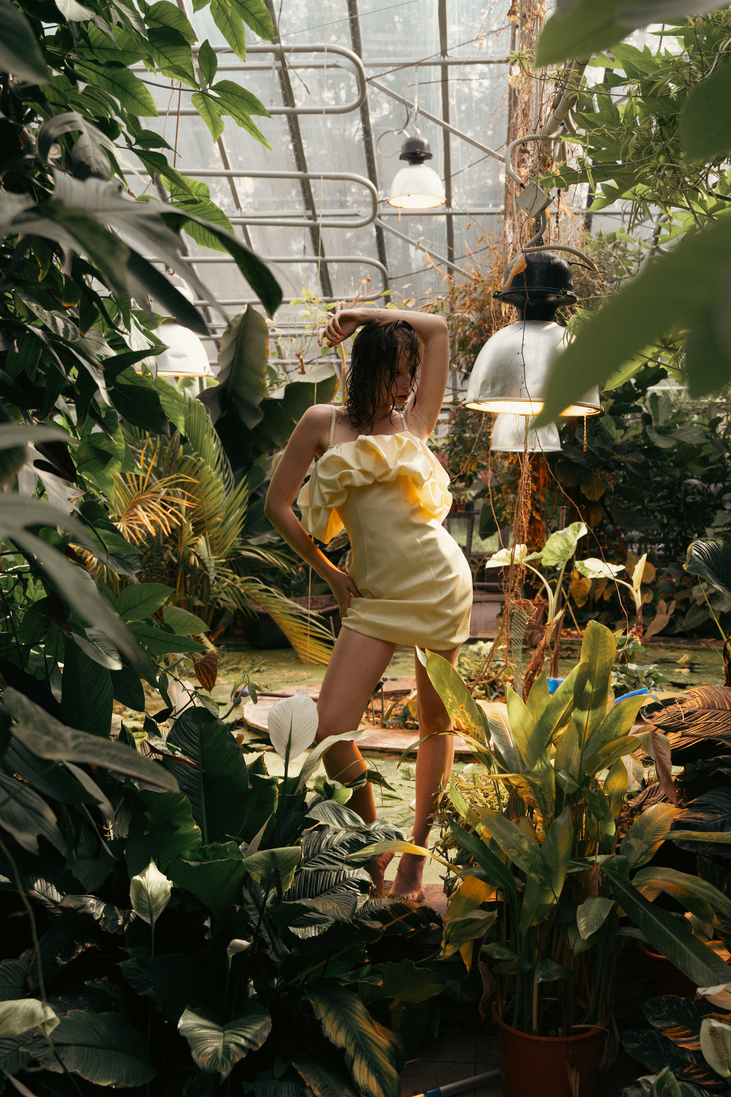 Fashion model in a cream dress posing among tropical plants in a greenhouse