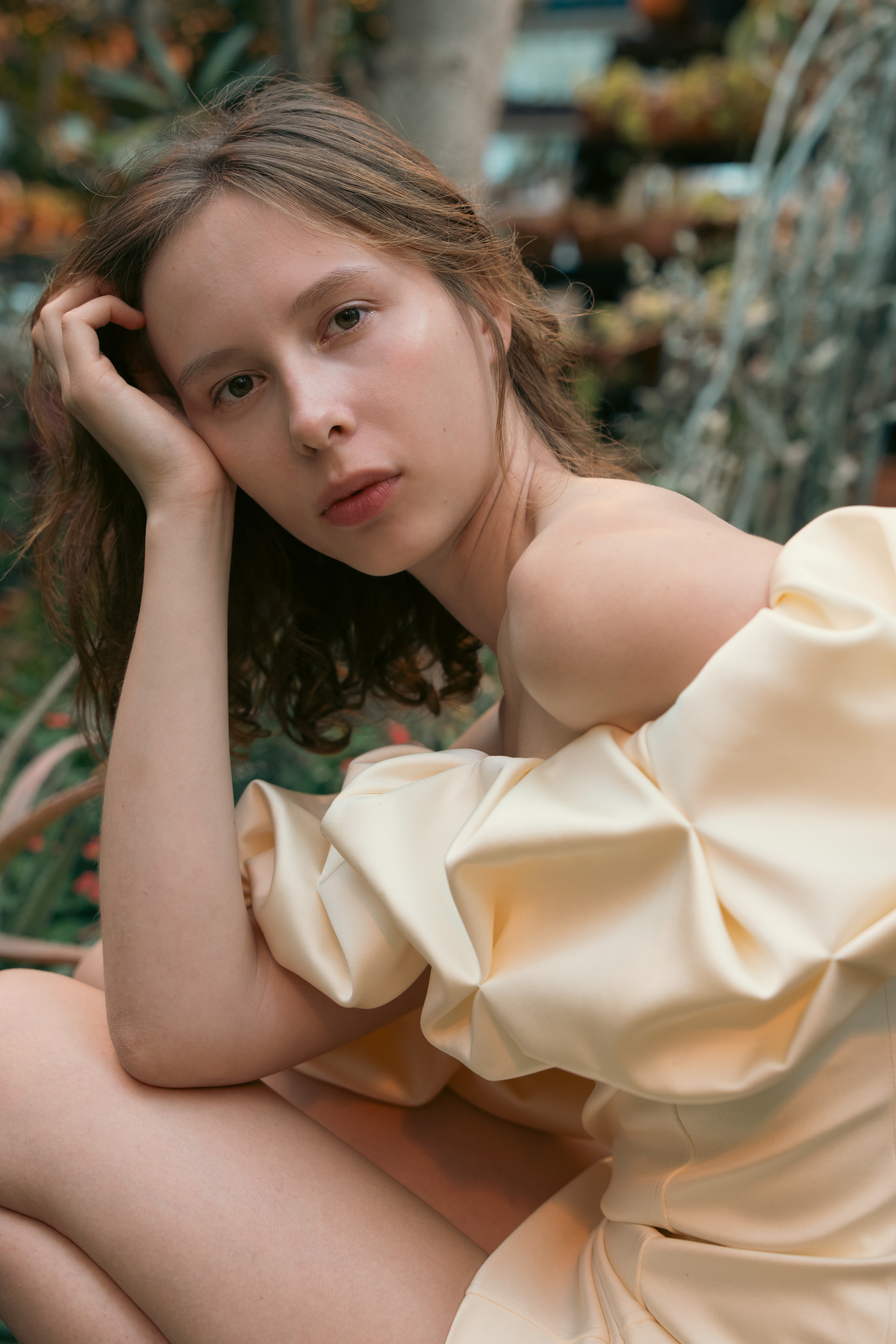 Editorial portrait of a woman in a cream dress surrounded by botanical greenery
