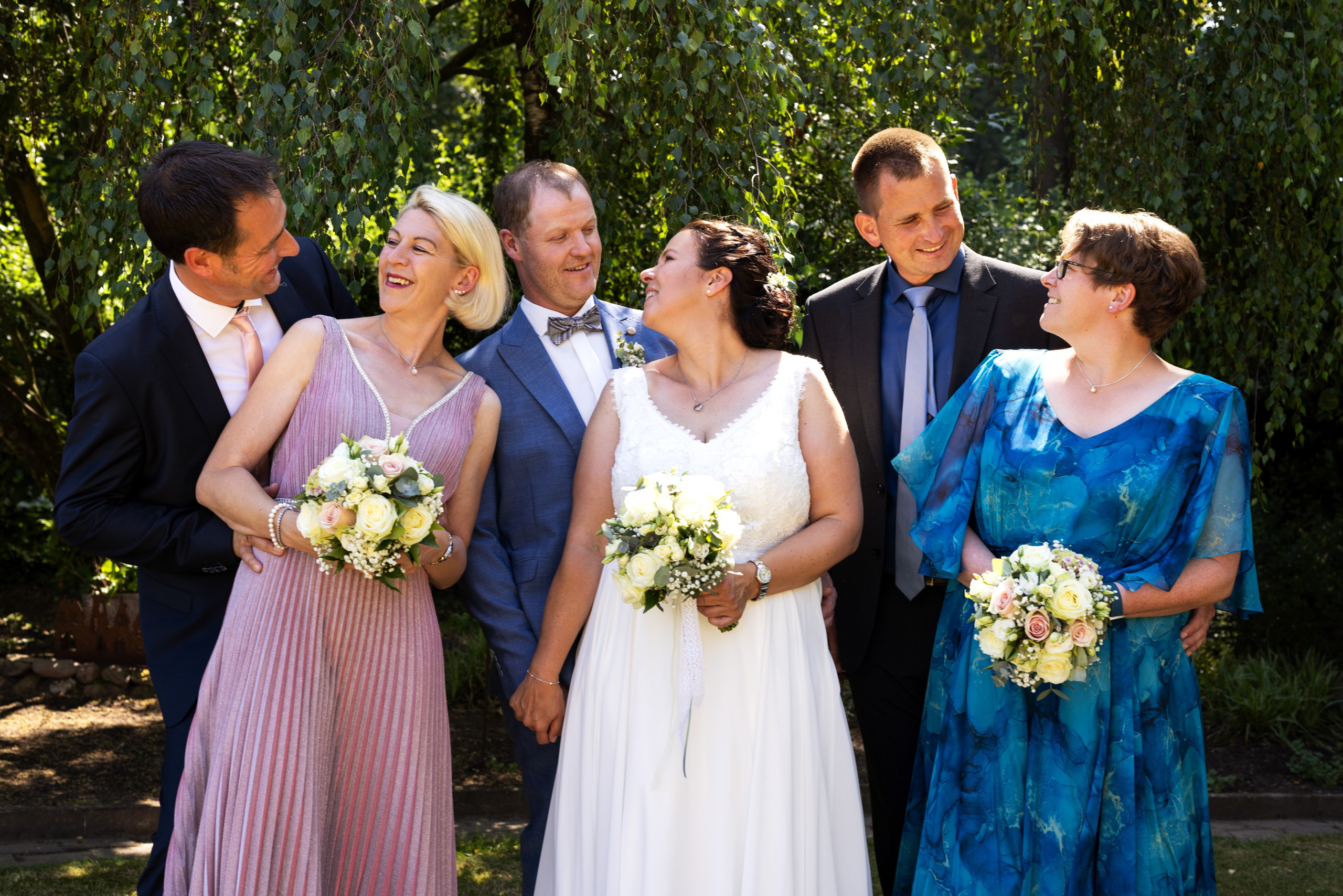 Gruppenfoto mit Brautpaar und Familie im weitläufigen Garten, fröhliche Hochzeit in Bippen.