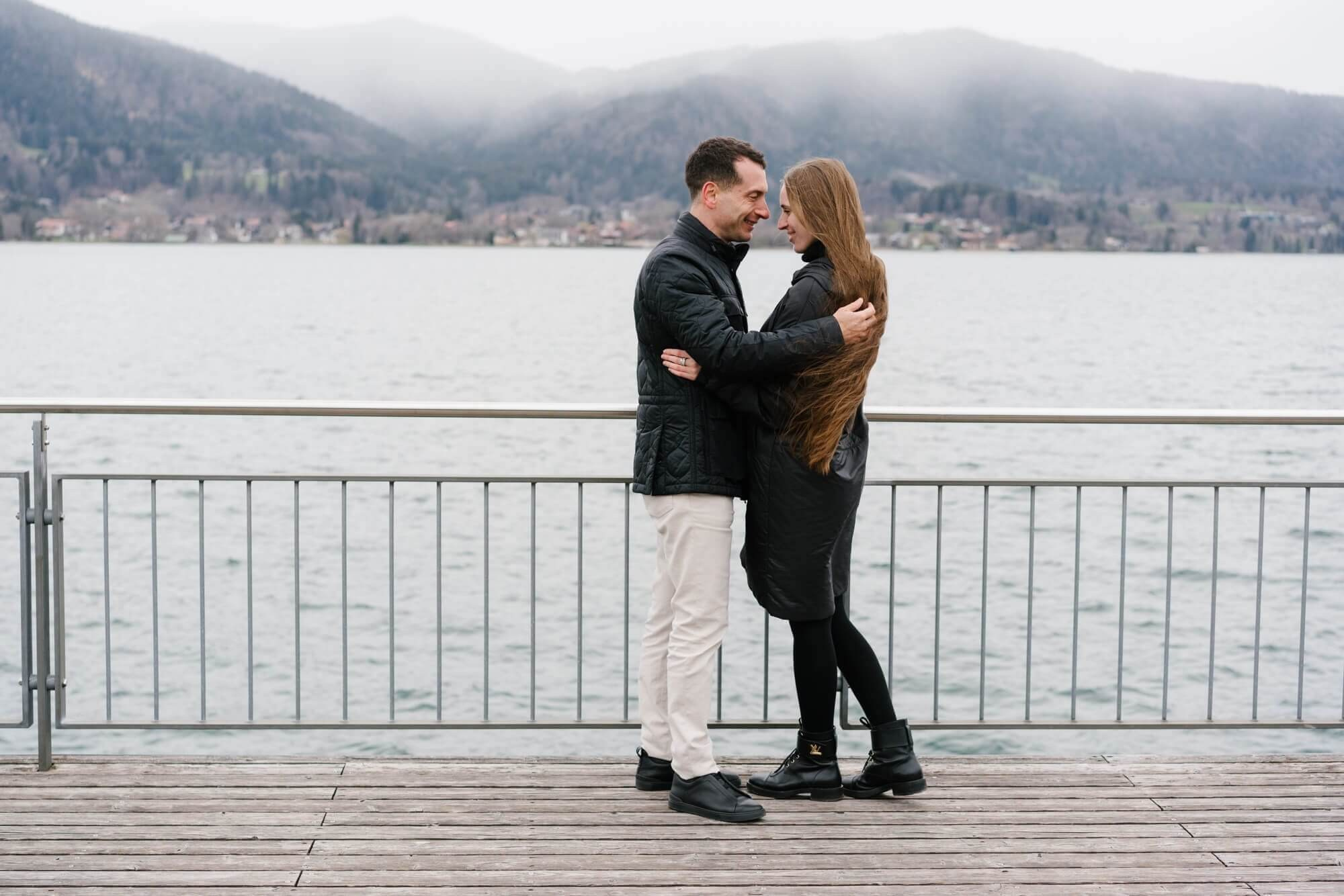 Couple close portrait on a dock at Tegernsee lake with misty mountains behind during couple photo session Germany