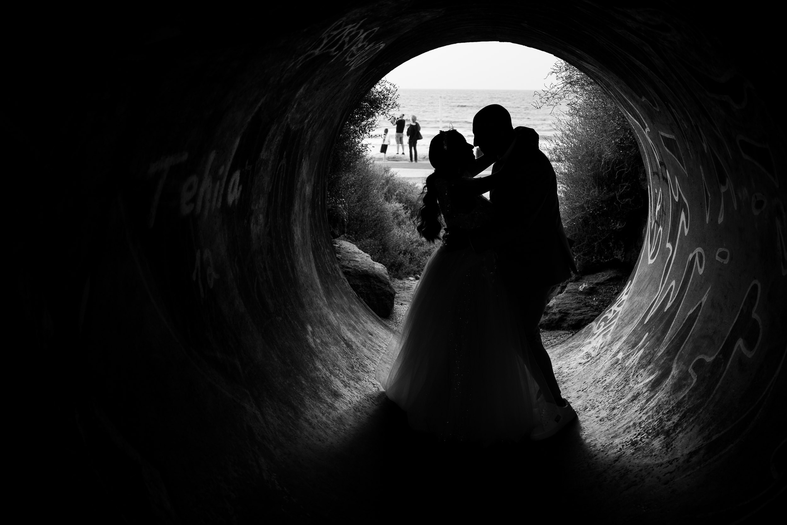 Black and white silhouette of a bride and groom embracing inside a tunnel overlooking the sea in Israel