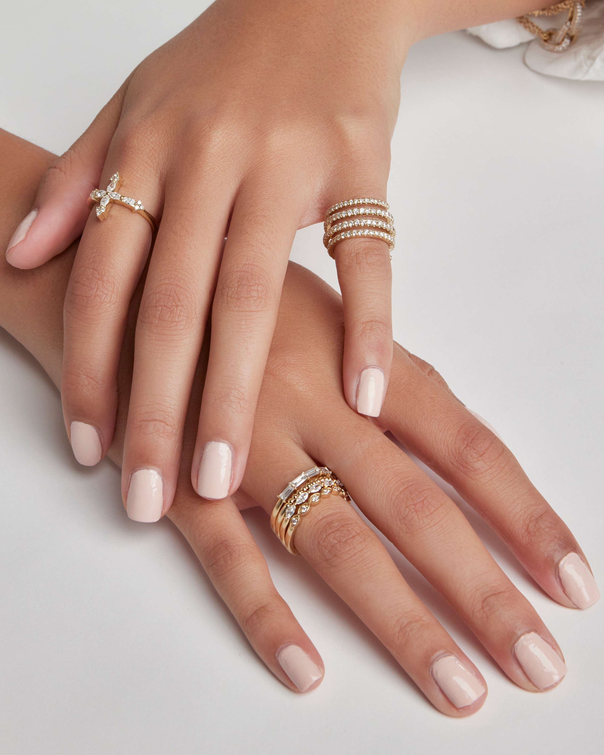 Manicured hands adorned with gold rings and bracelets, showcasing a sophisticated jewelry collection.