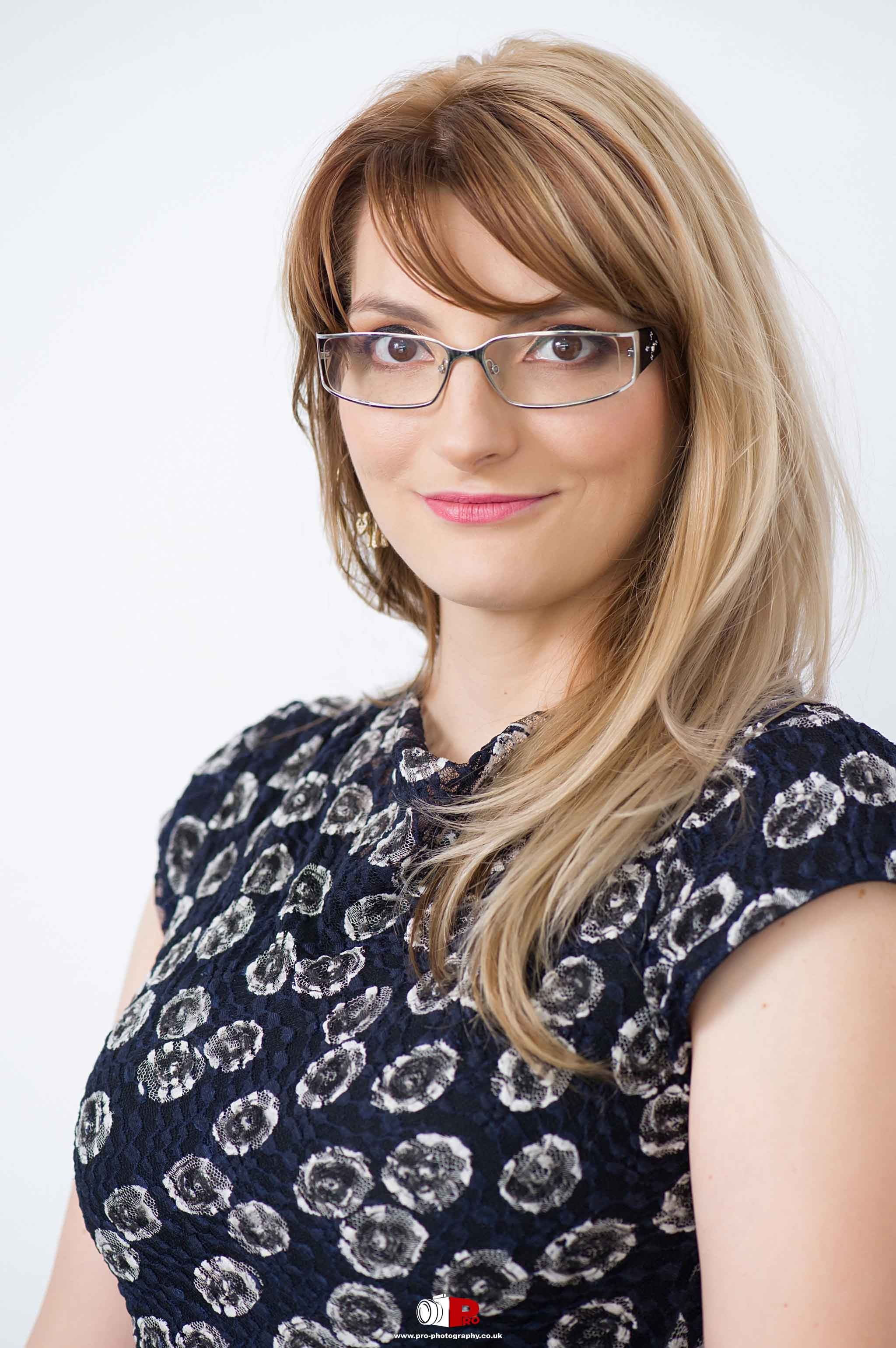 A smiling woman with glasses in a floral top, posing for a professional headshot on a white background.