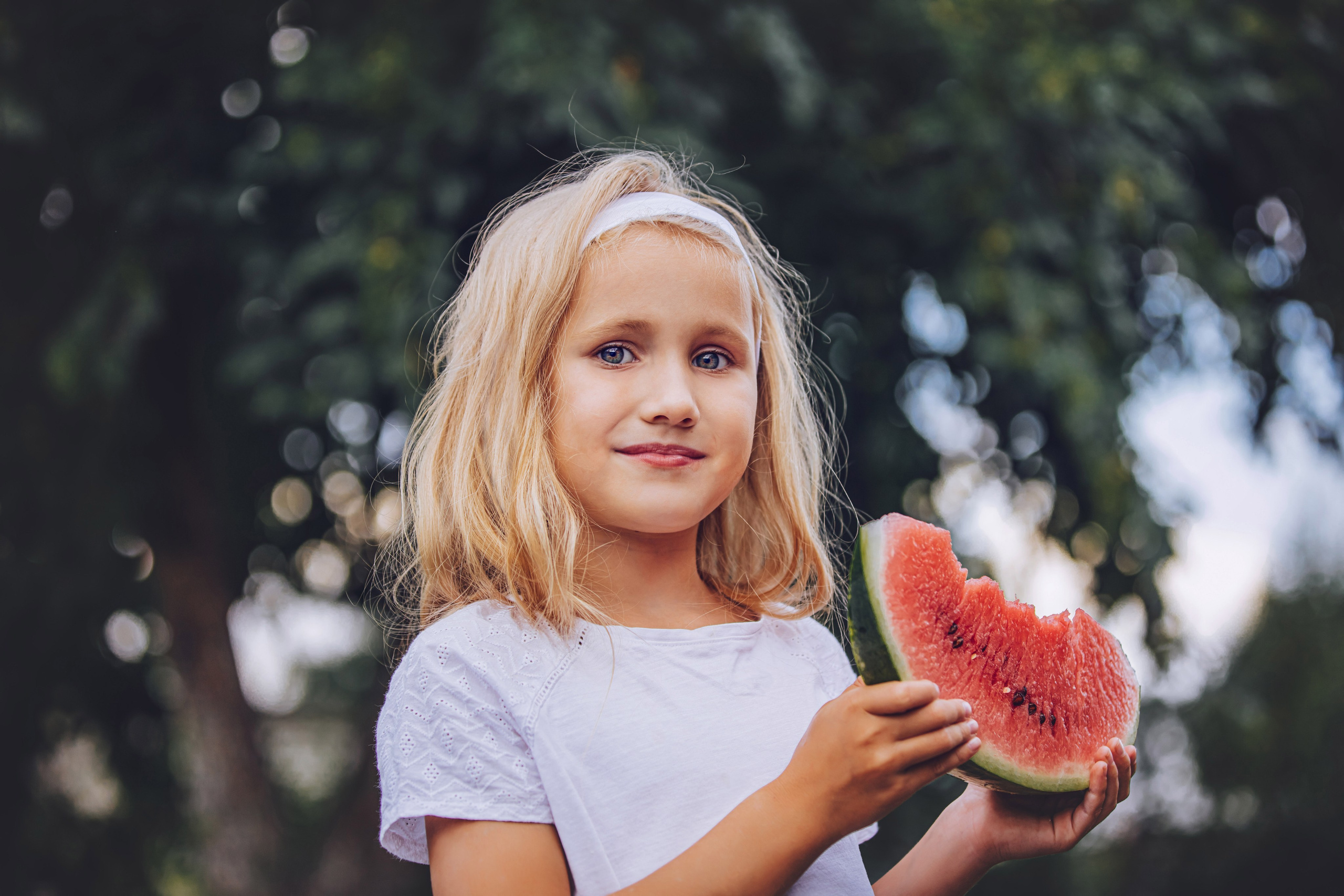 Fillette blonde mangeant une tranche de pastèque en été, regard doux vers l'objectif