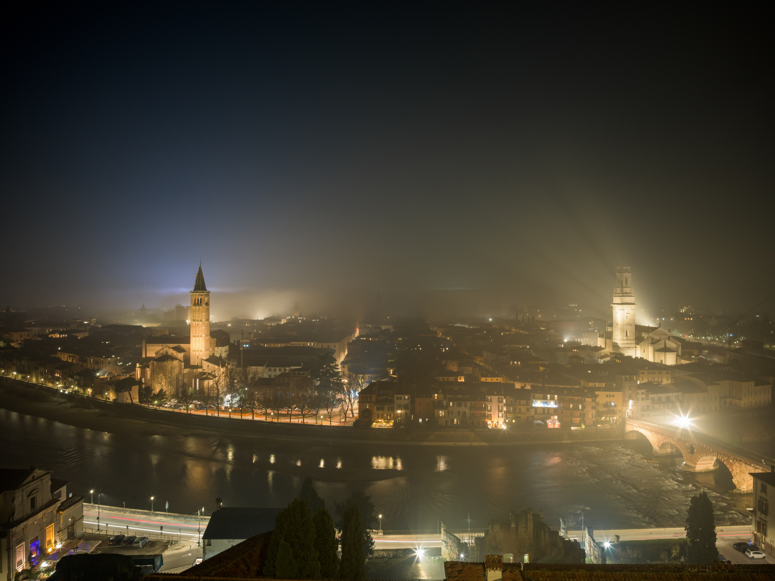 A dramatic night panorama of Verona illuminated by city lights and mist. Cinematic fine art photography capturing scale, atmosphere and timeless architecture.