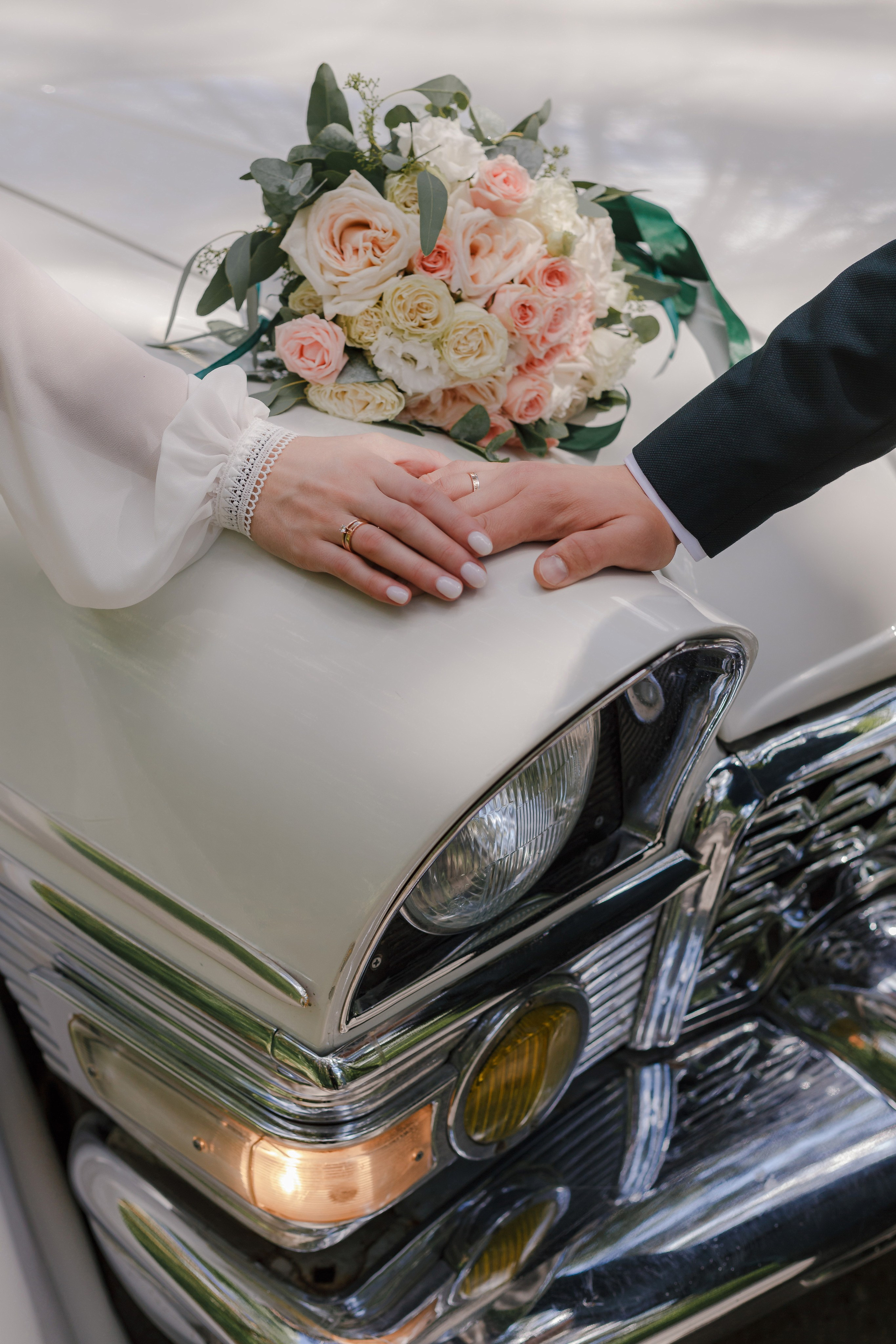 manos de la novia y el novio en el fondo de un ramo de novia y un auto viejo